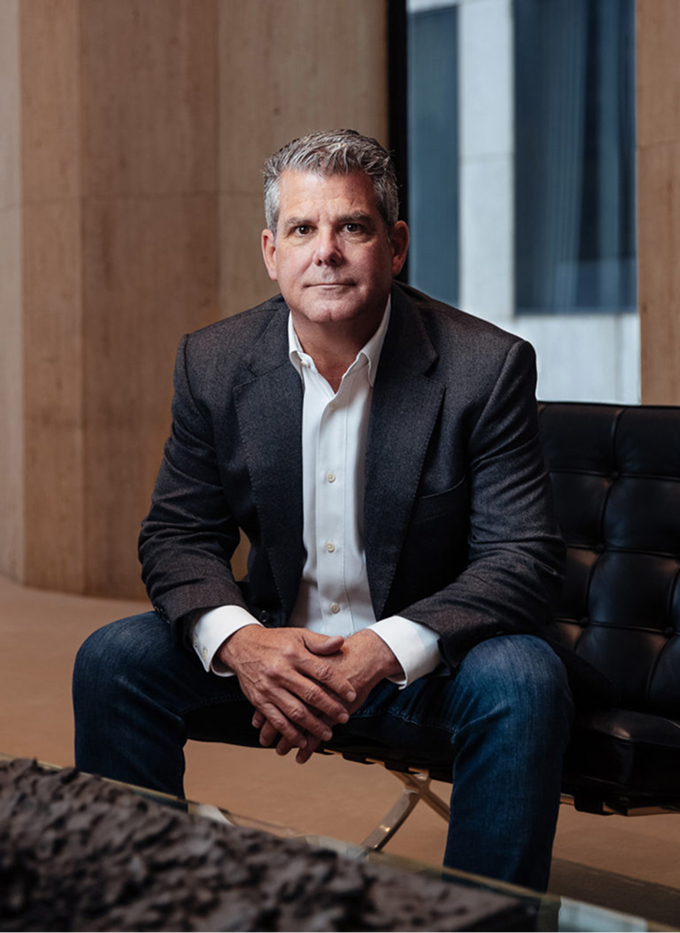 Image of Trey Trahan seated on barcelona chair with travertine marble wall behind him.