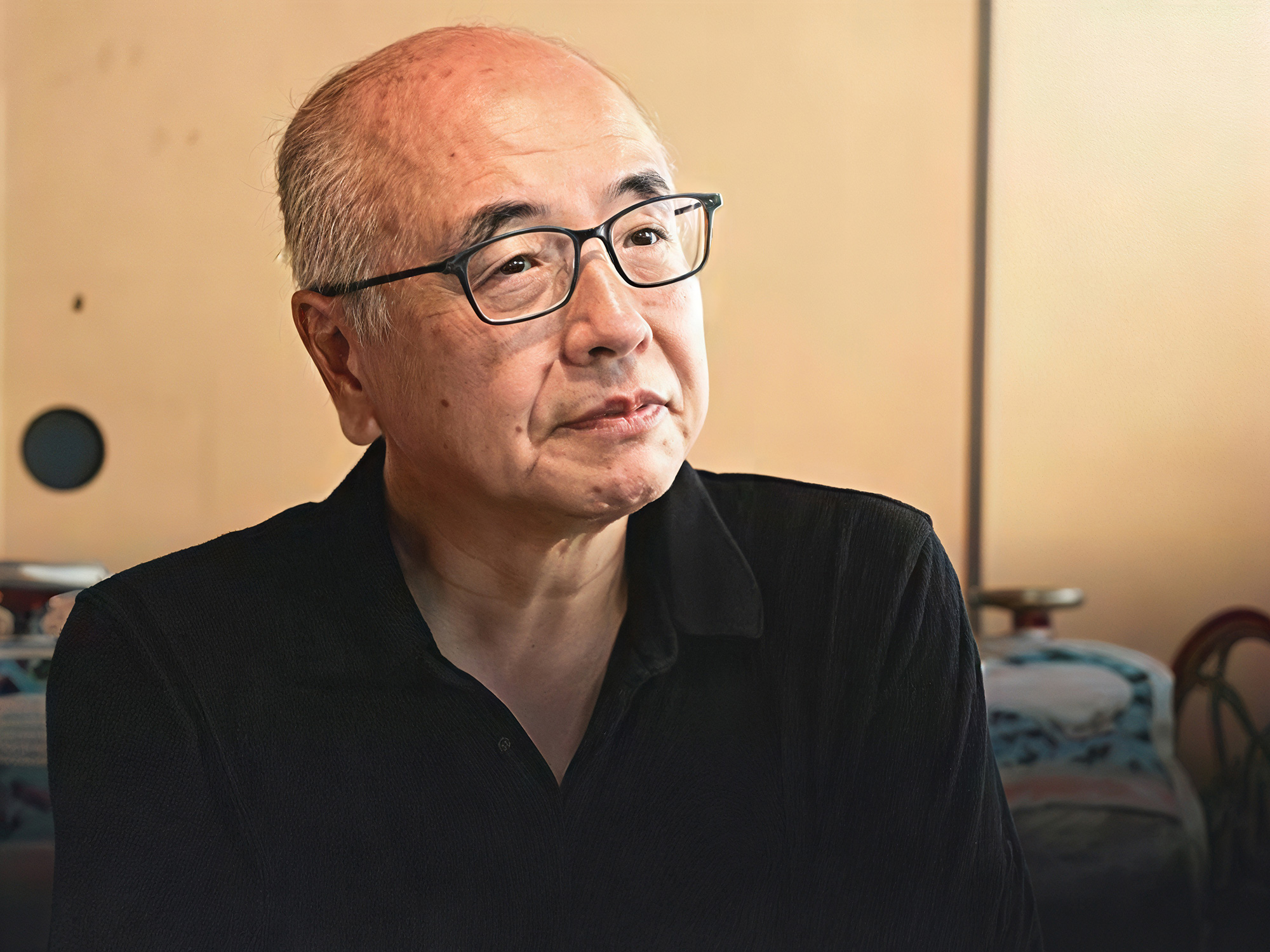 Portrait of a Japanese ceramic artist Yagi Akira wearing glasses, seated indoors in soft natural...