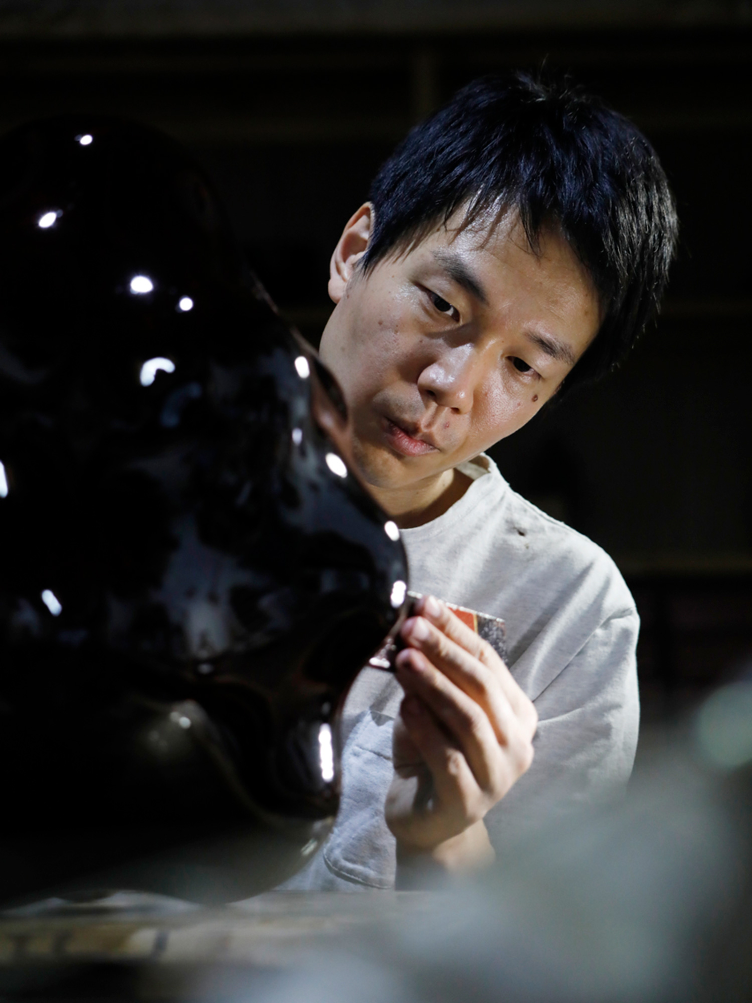 Japanese lacquer artist Genta Ishizuka carefully refining a dark lacquer sculptural form, highlighting...