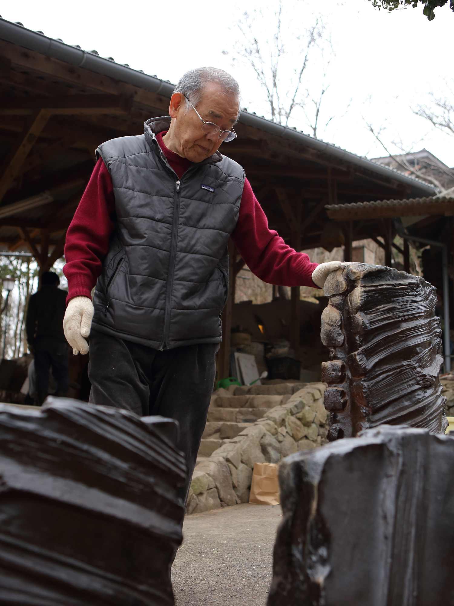 Japanese ceramic artist Jun Isezaki examining large wood-fired ceramic sculptures outdoors near...