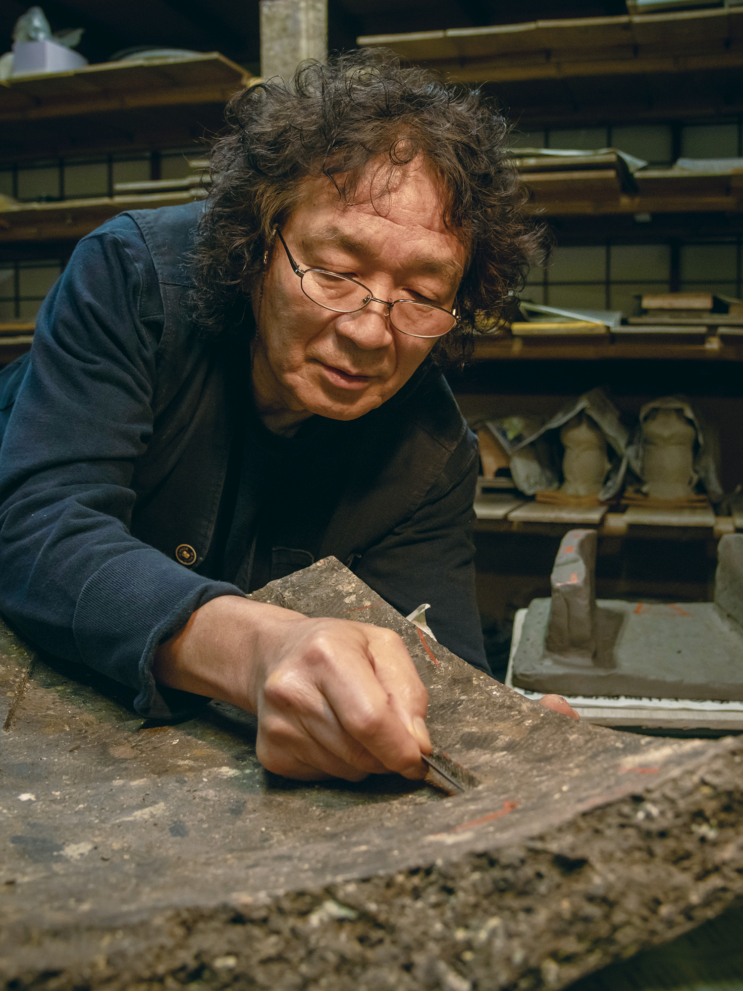 Studio scene of Japanese artist Ryuichi Kakurezaki meticulously carving a textured clay slab, highlighting...