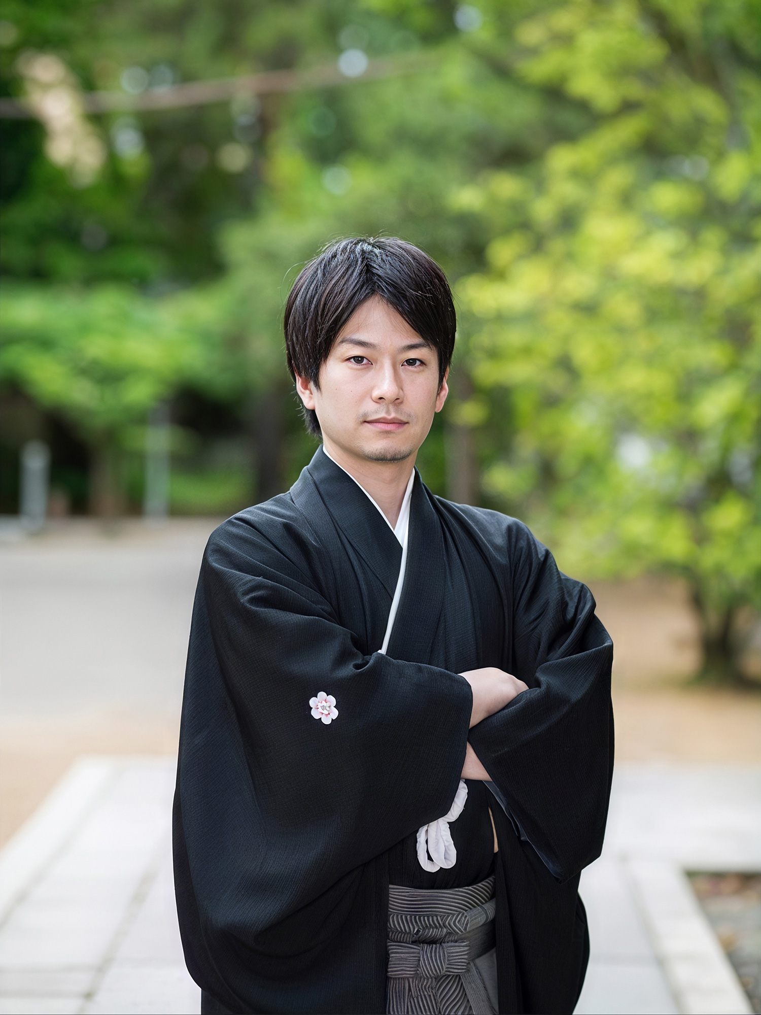 Outdoor portrait of Raku XVI dressed in formal Japanese kimono attire against a lush green background.