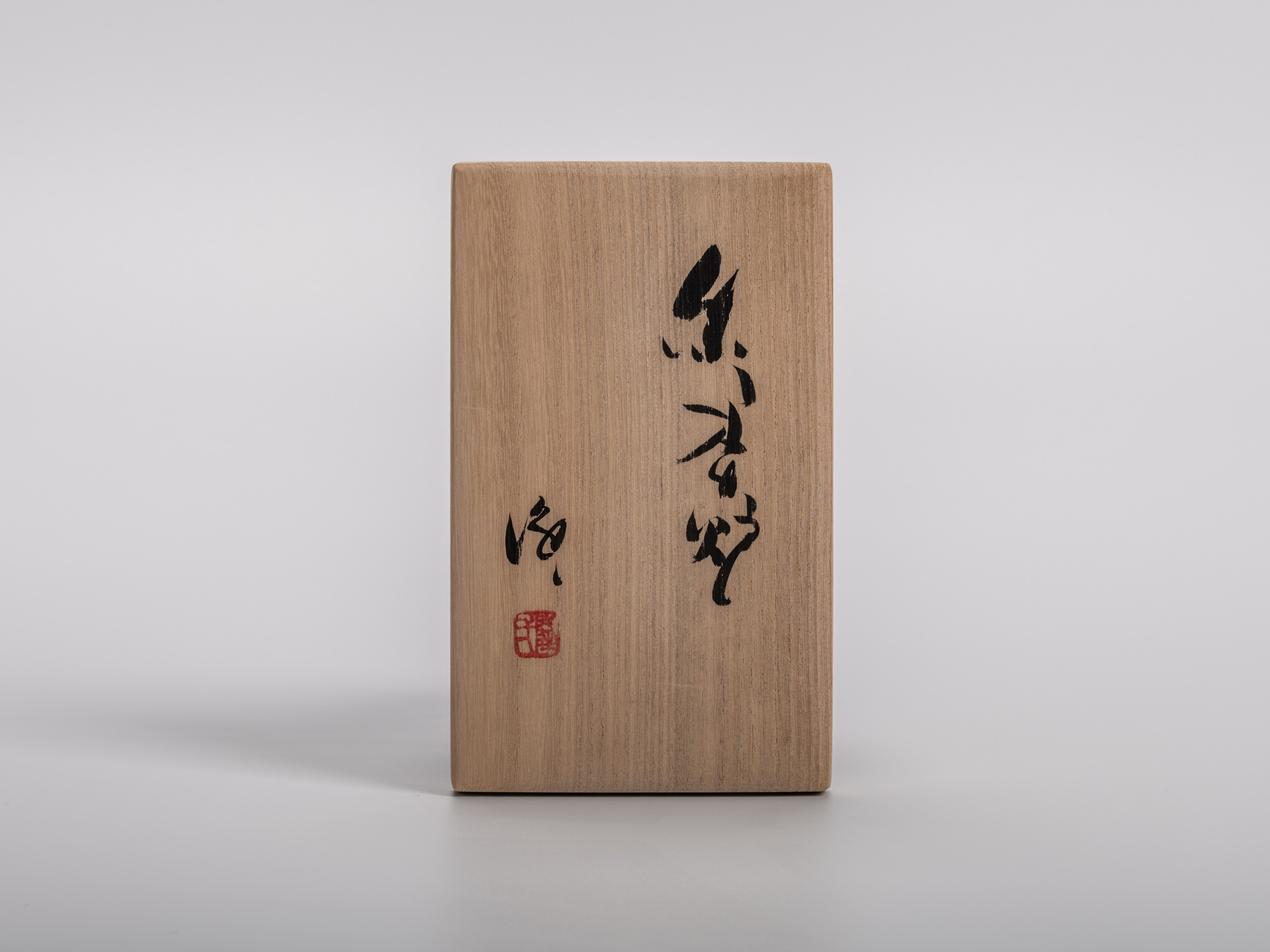 A vertical close-up shot of the front of a light brown, rectangular wooden box against a plain...