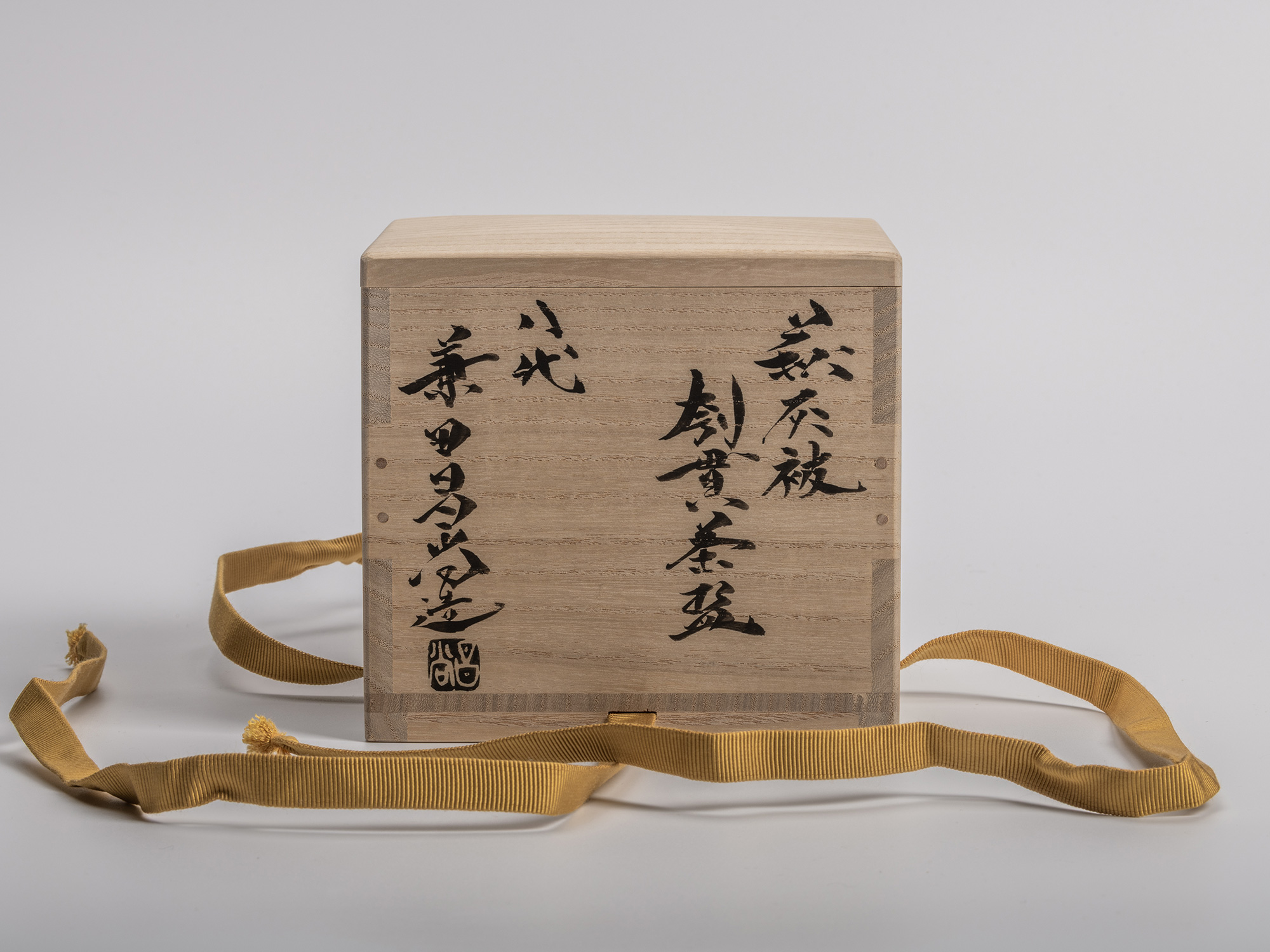 Wooden box for Masanao Kaneta’s Haikaburi Kurinuki tea bowl, shown with untied mustard yellow cord...