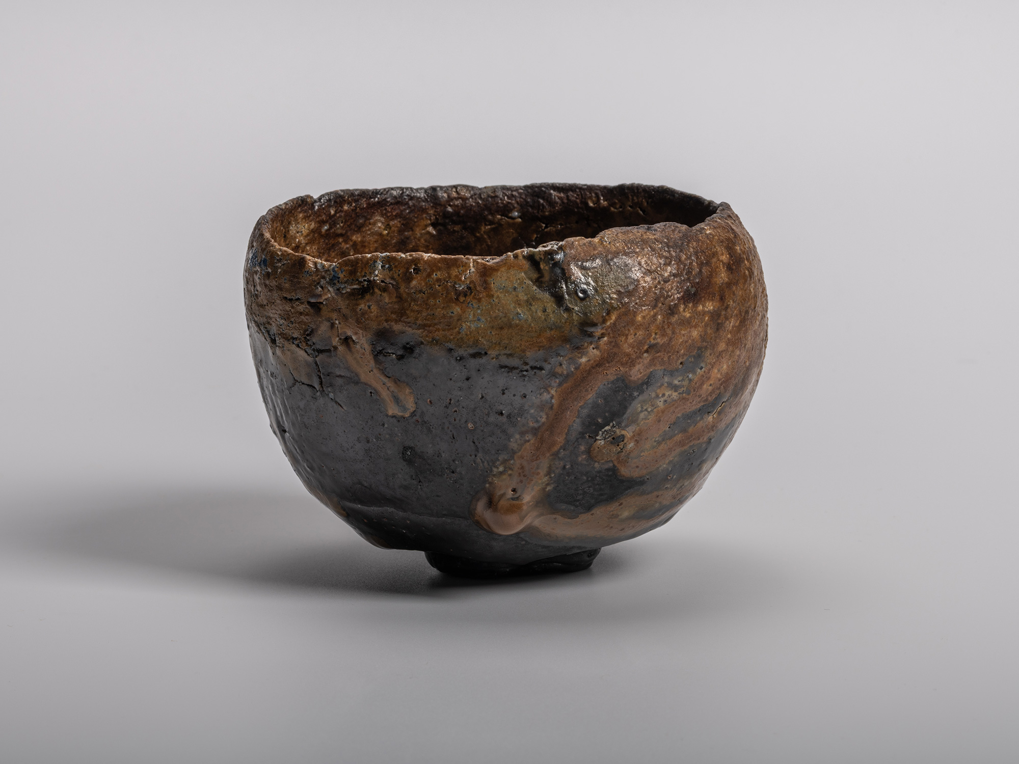 A profile view of a sculptural Konko black tea bowl by Ryuichi Kakurezaki featuring a heavily textured,...