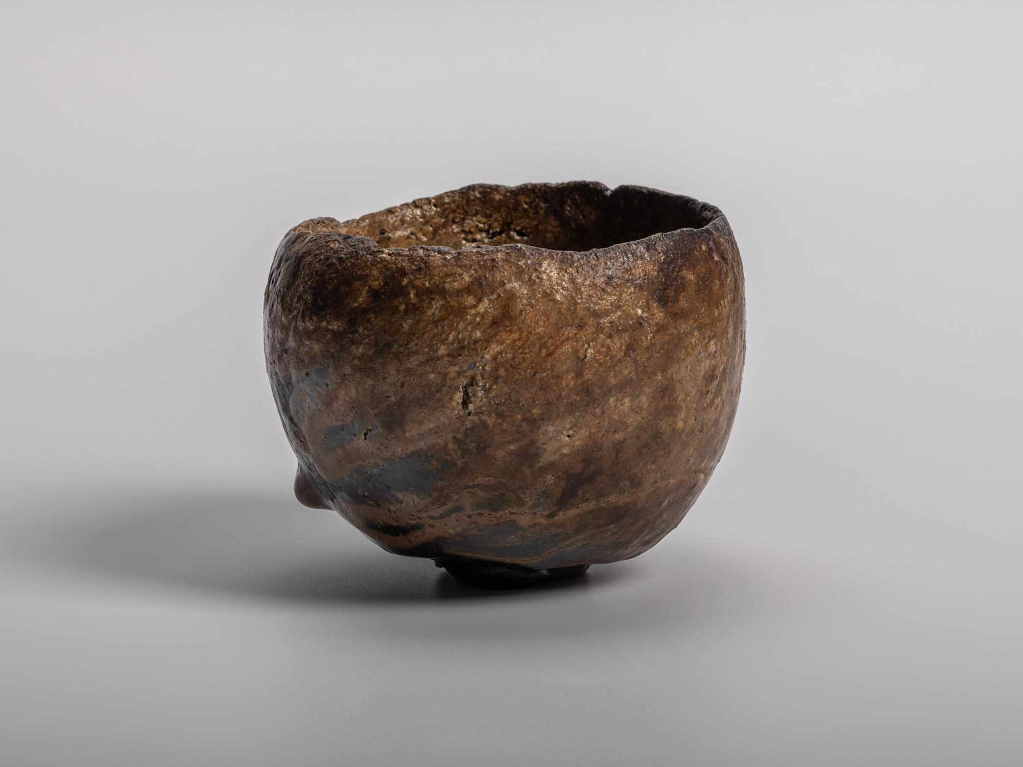 A profile view of a sculptural Konko black tea bowl by Ryuichi Kakurezaki featuring a heavily textured,...