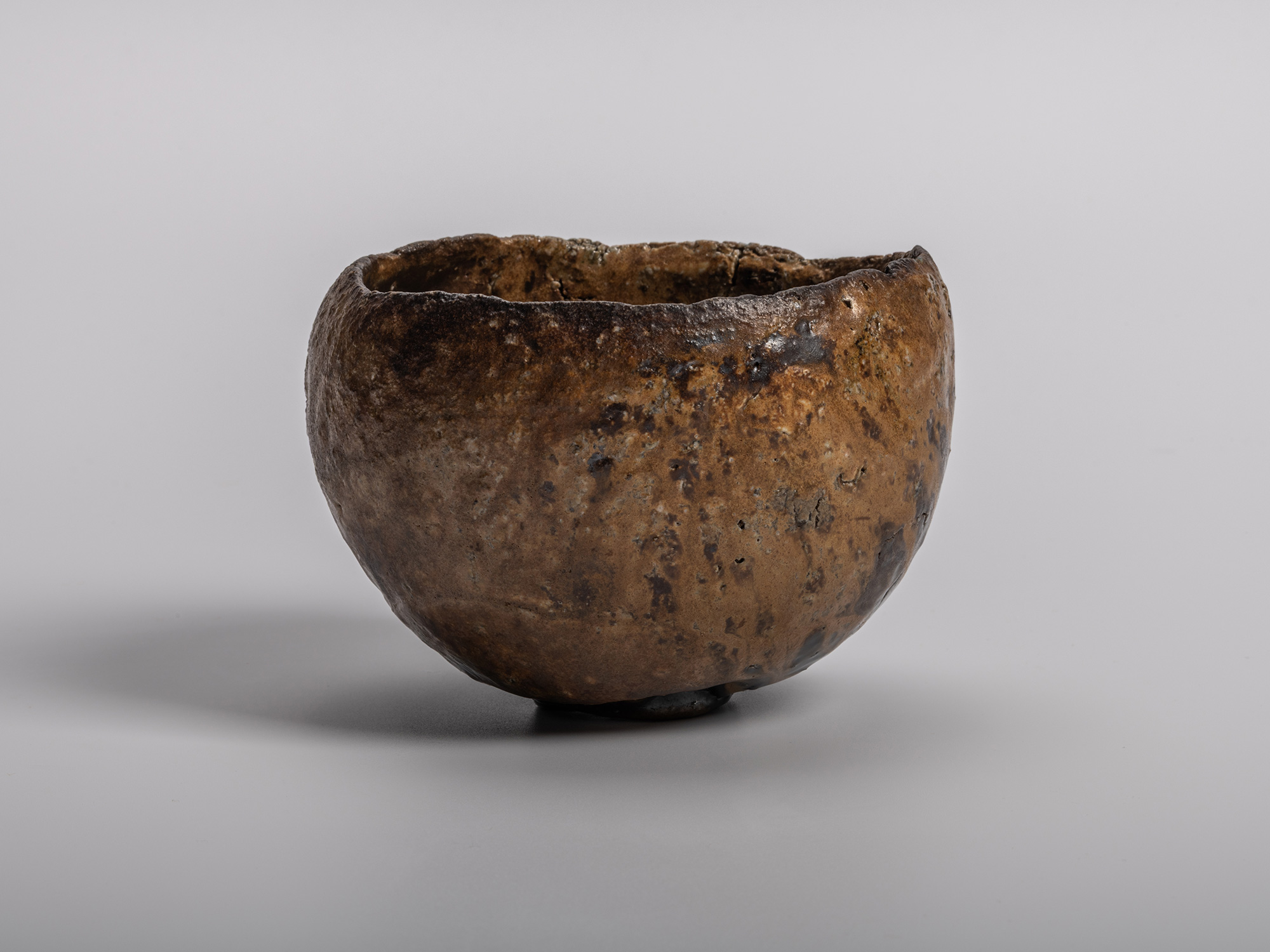 A profile view of a sculptural Konko black tea bowl by Ryuichi Kakurezaki featuring a heavily textured,...