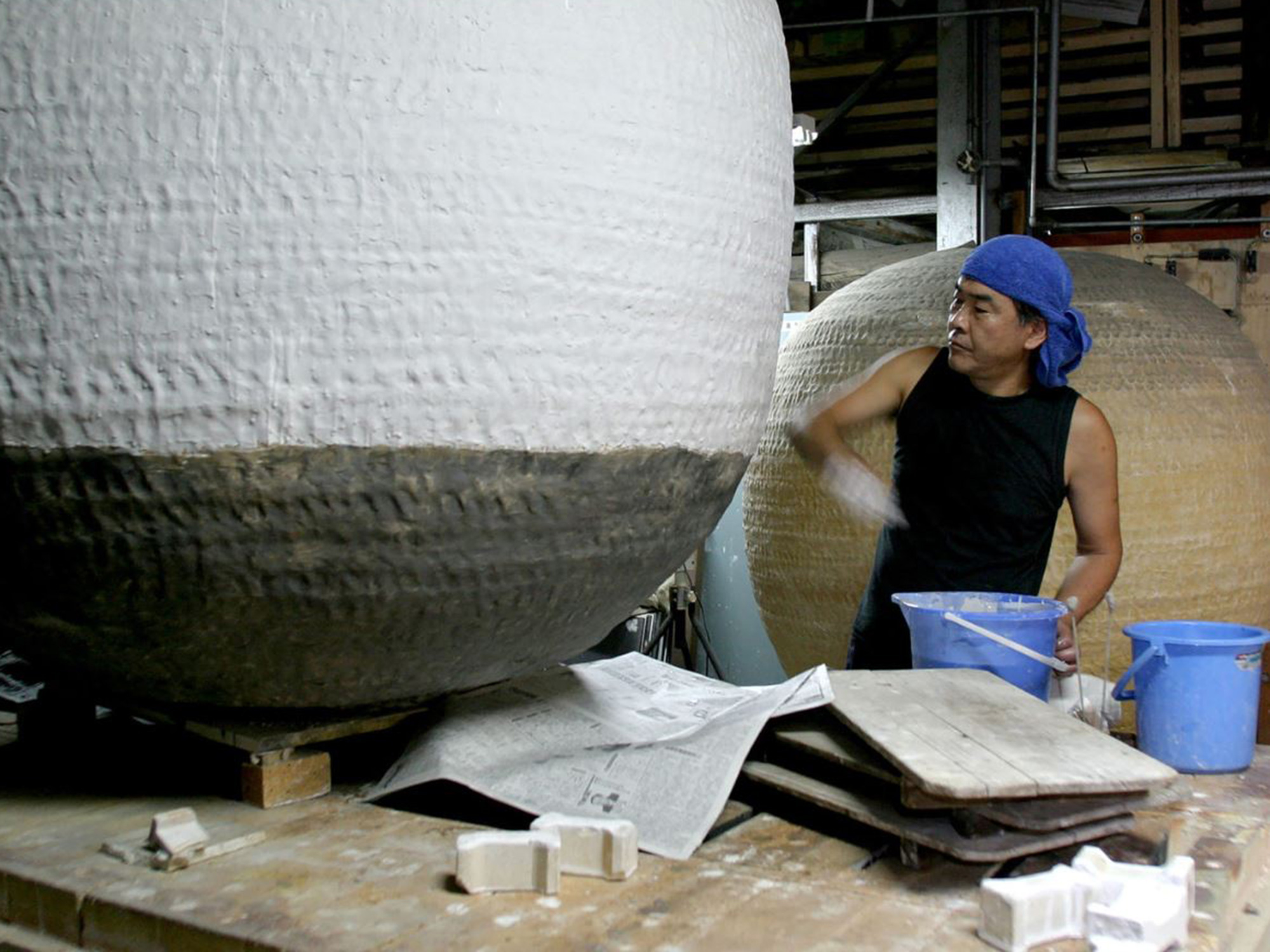Japanese artist Masamichi Yoshikawa applying slip to a large spherical ceramic vessel in a studio...