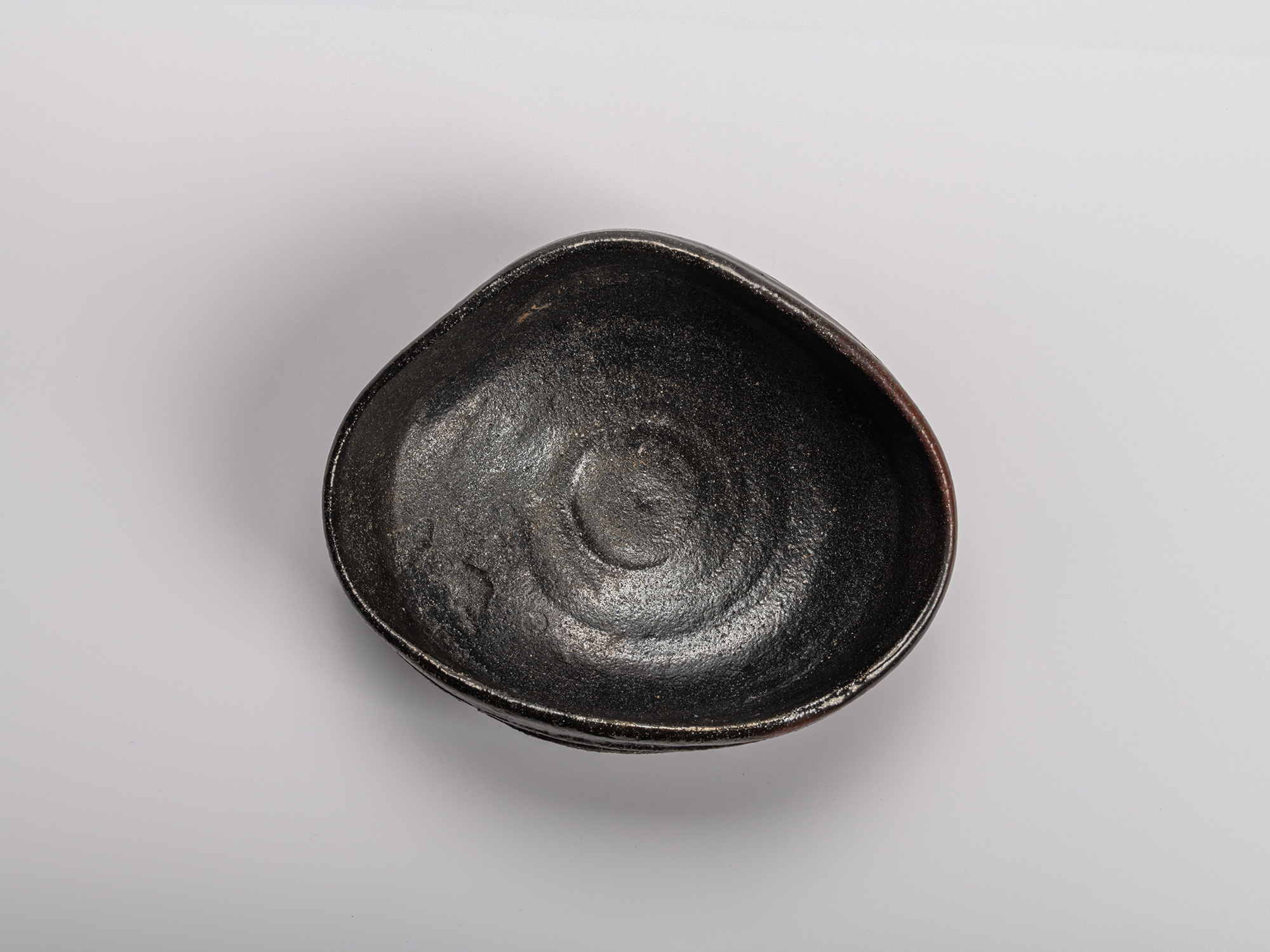 Interior (mikomi) of Shiro Tsujimura’s Oribe Kuro Chawan, showing the soft oval form, textured...