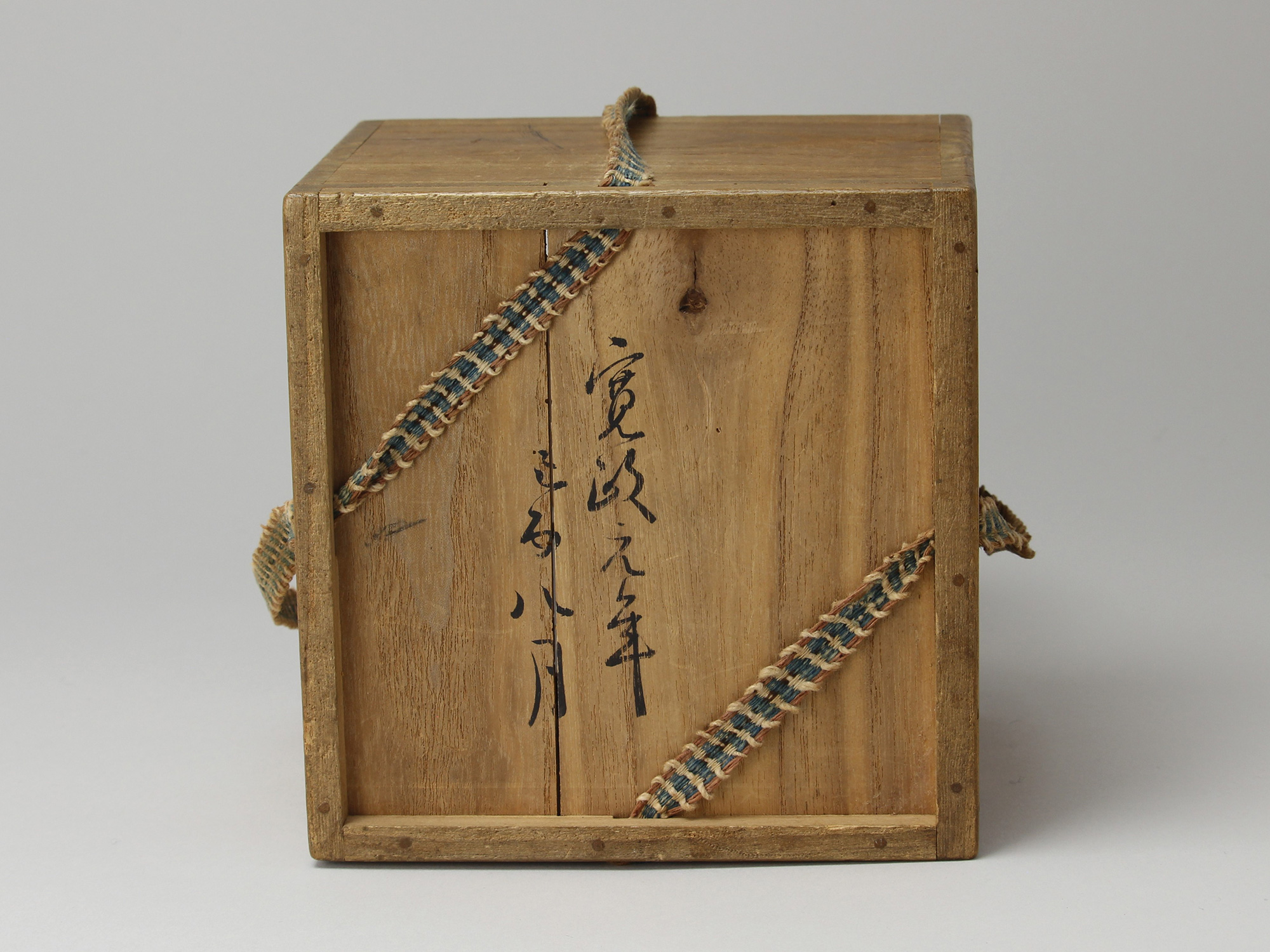 Bottom view of a paulownia wood storage box (tomobako) showing two columns of hand-brushed sumi...