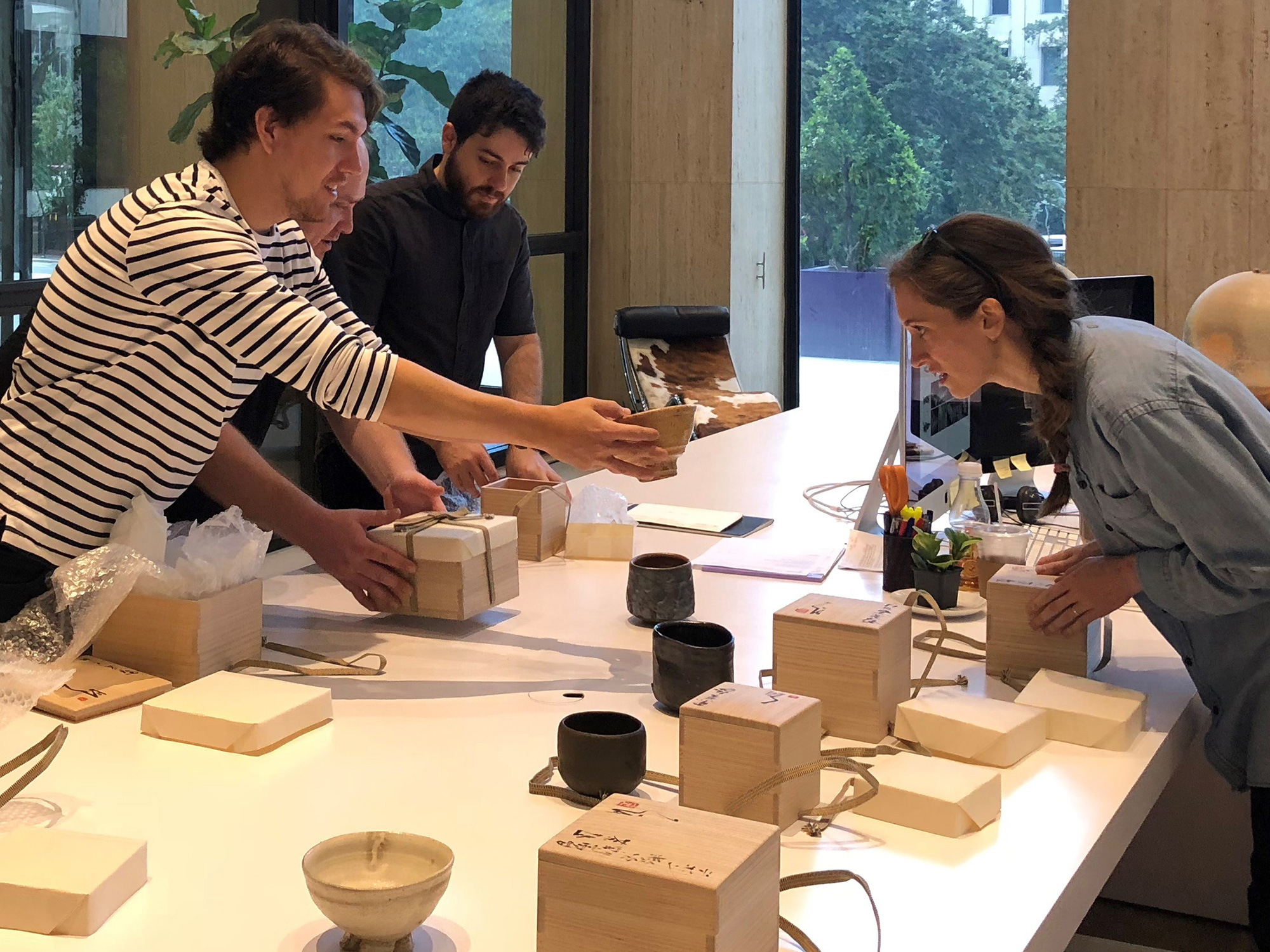 Staff unboxing and examining handcrafted tea bowls by Tsujimura in an office setting.