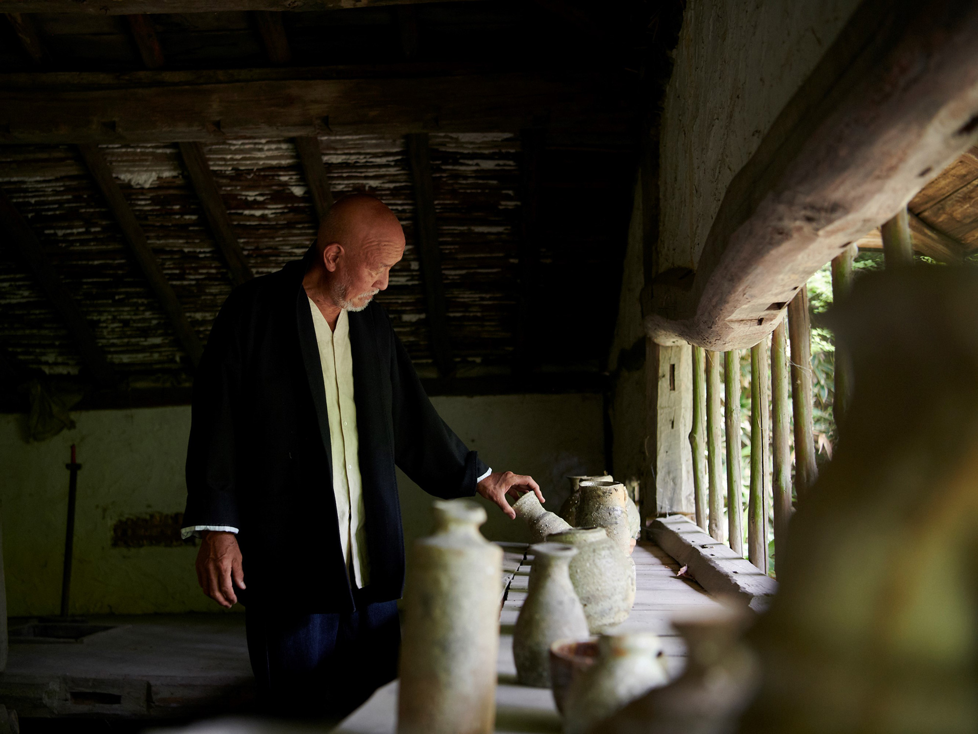 Shiro Tsujimura, master ceramic artist, standing in a historic Japanese thatched-roof house as...