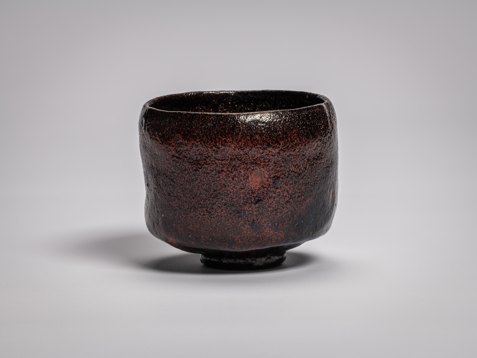 Black Raku tea bowl by Raku Ichinyū IV, featuring a subtly irregular cylindrical form, dark iron-rich...