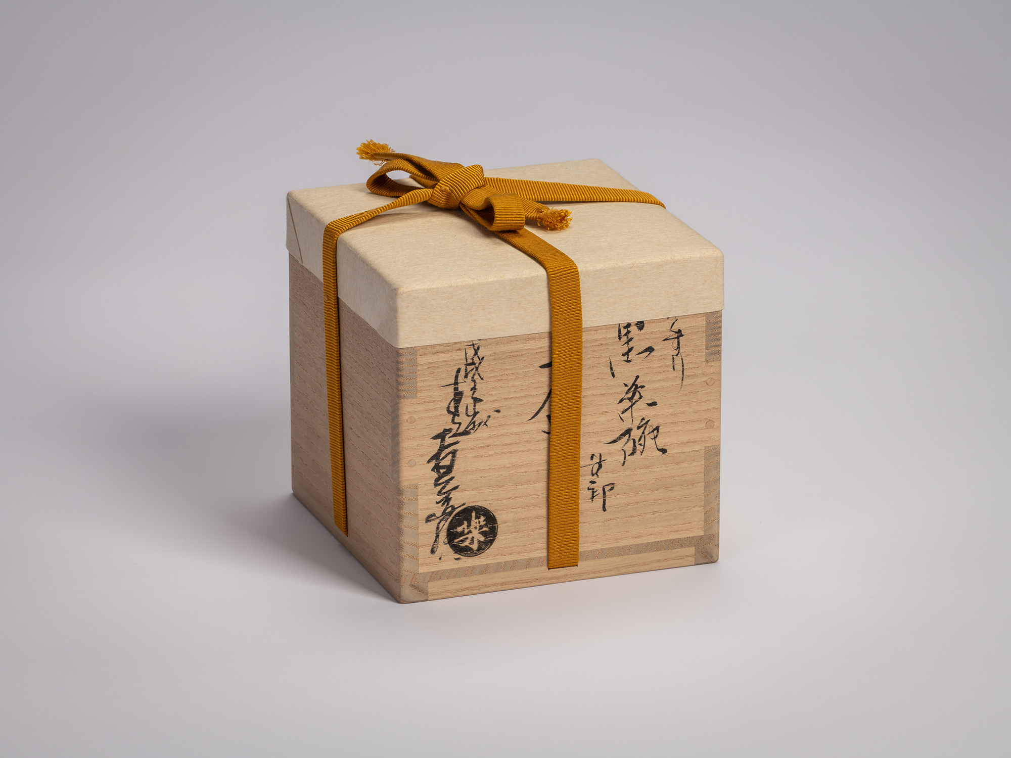 Wooden tomobako box for a Black Raku tea bowl by Raku Ichinyū IV, shown with its mustard cloth...