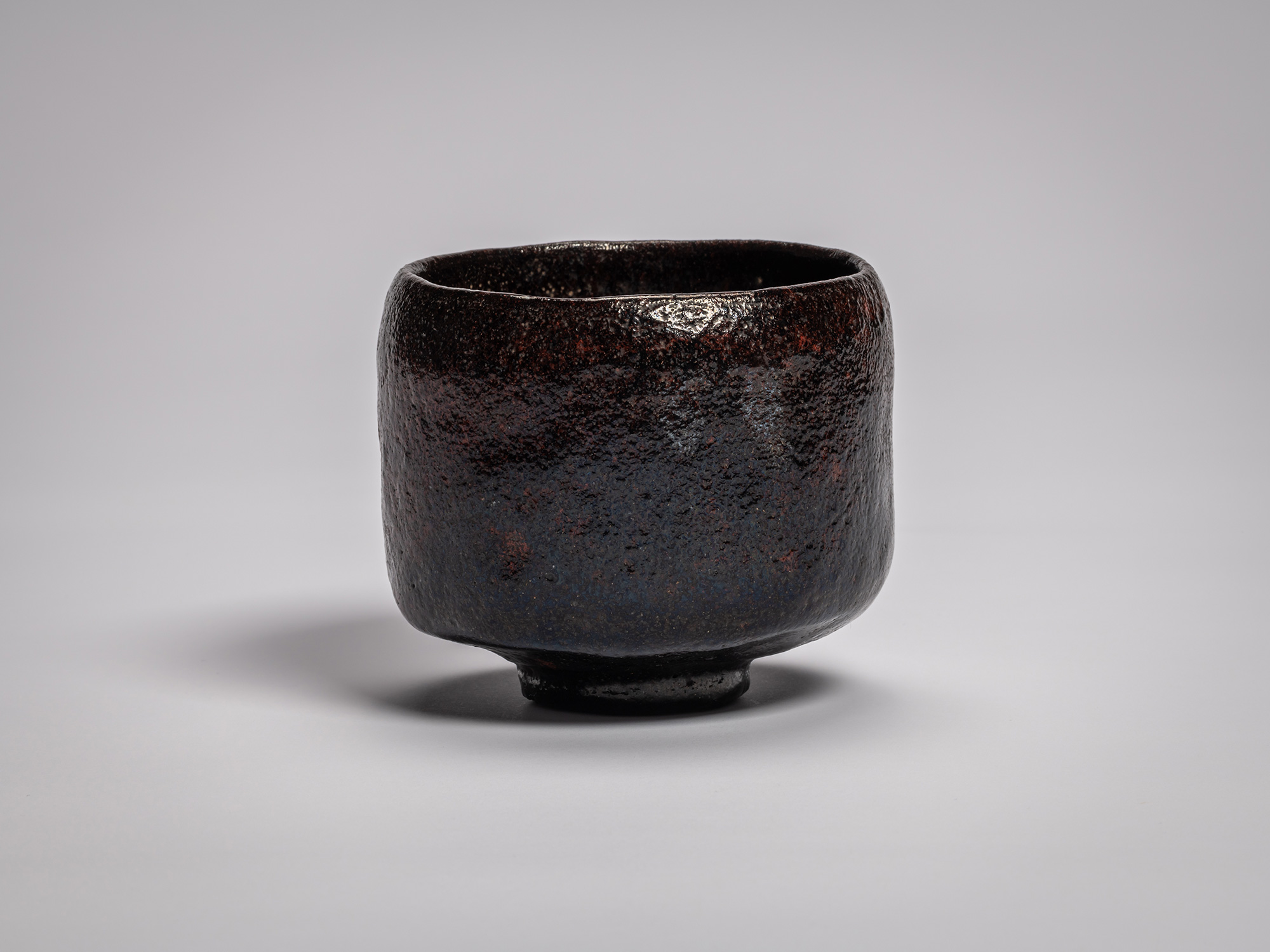 Black Raku tea bowl by Raku Ichinyū IV, featuring a subtly irregular cylindrical form, dark iron-rich...