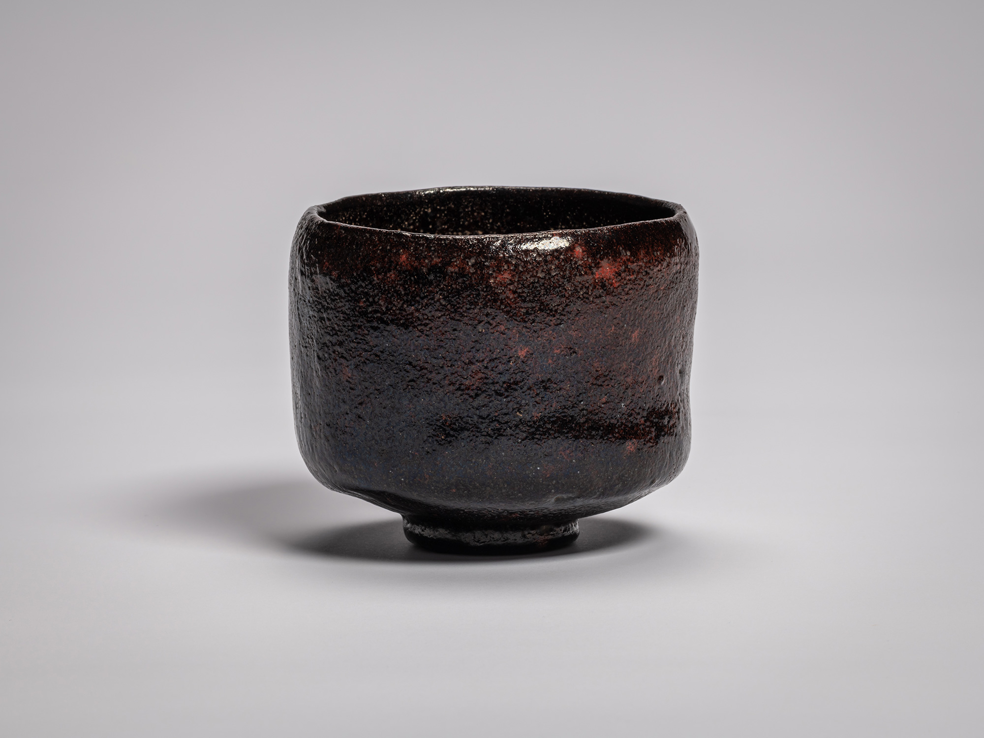 Black Raku tea bowl by Raku Ichinyū IV, featuring a subtly irregular cylindrical form, dark iron-rich...