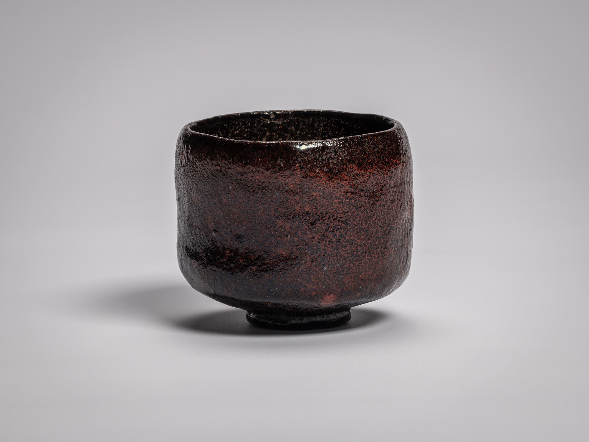 Black Raku tea bowl by Raku Ichinyū IV, featuring a subtly irregular cylindrical form, dark iron-rich...