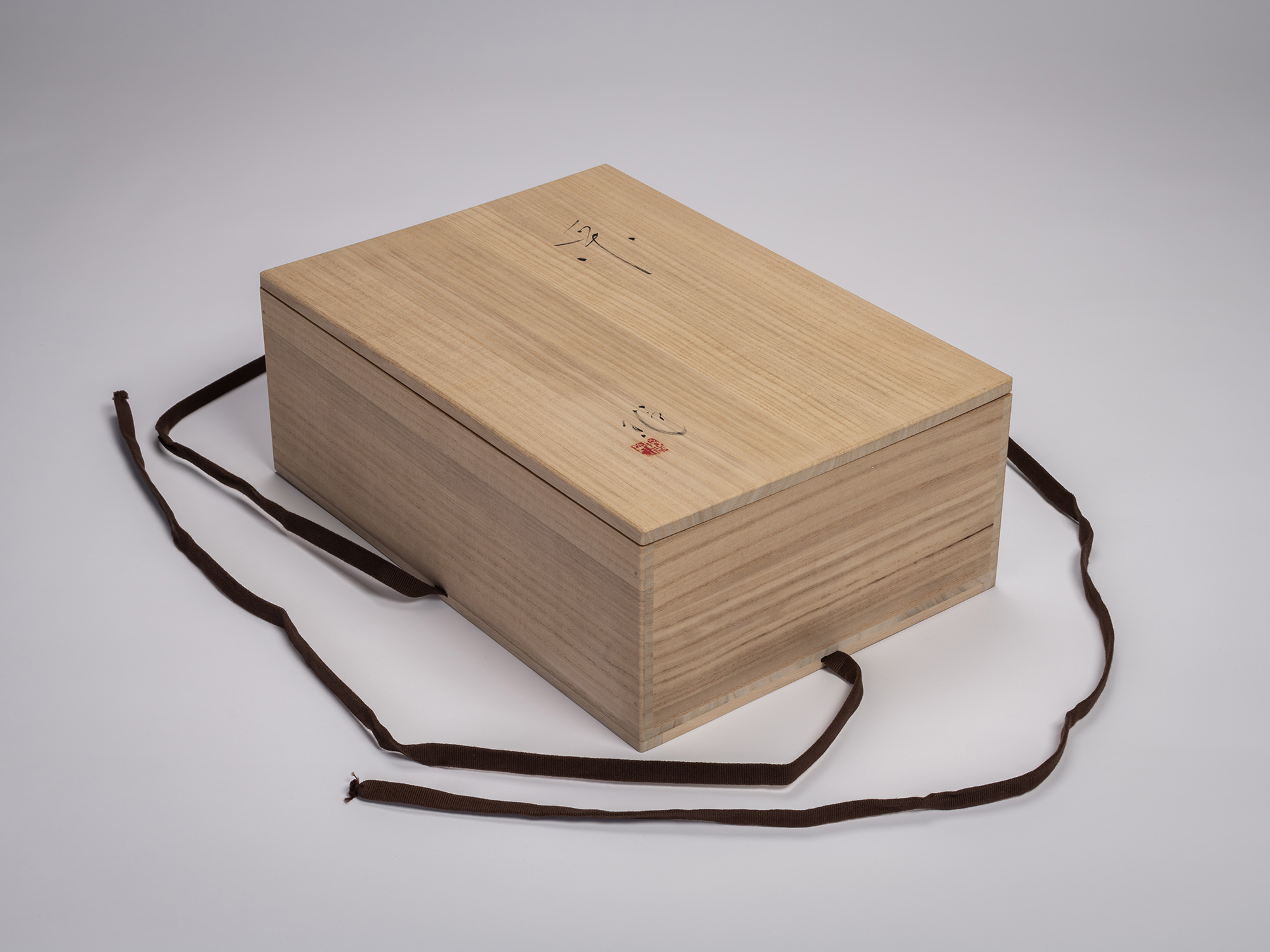 Angled view of a wooden tomobako storage box for Étranger by Aki Rusu, made of pale kiri wood with...