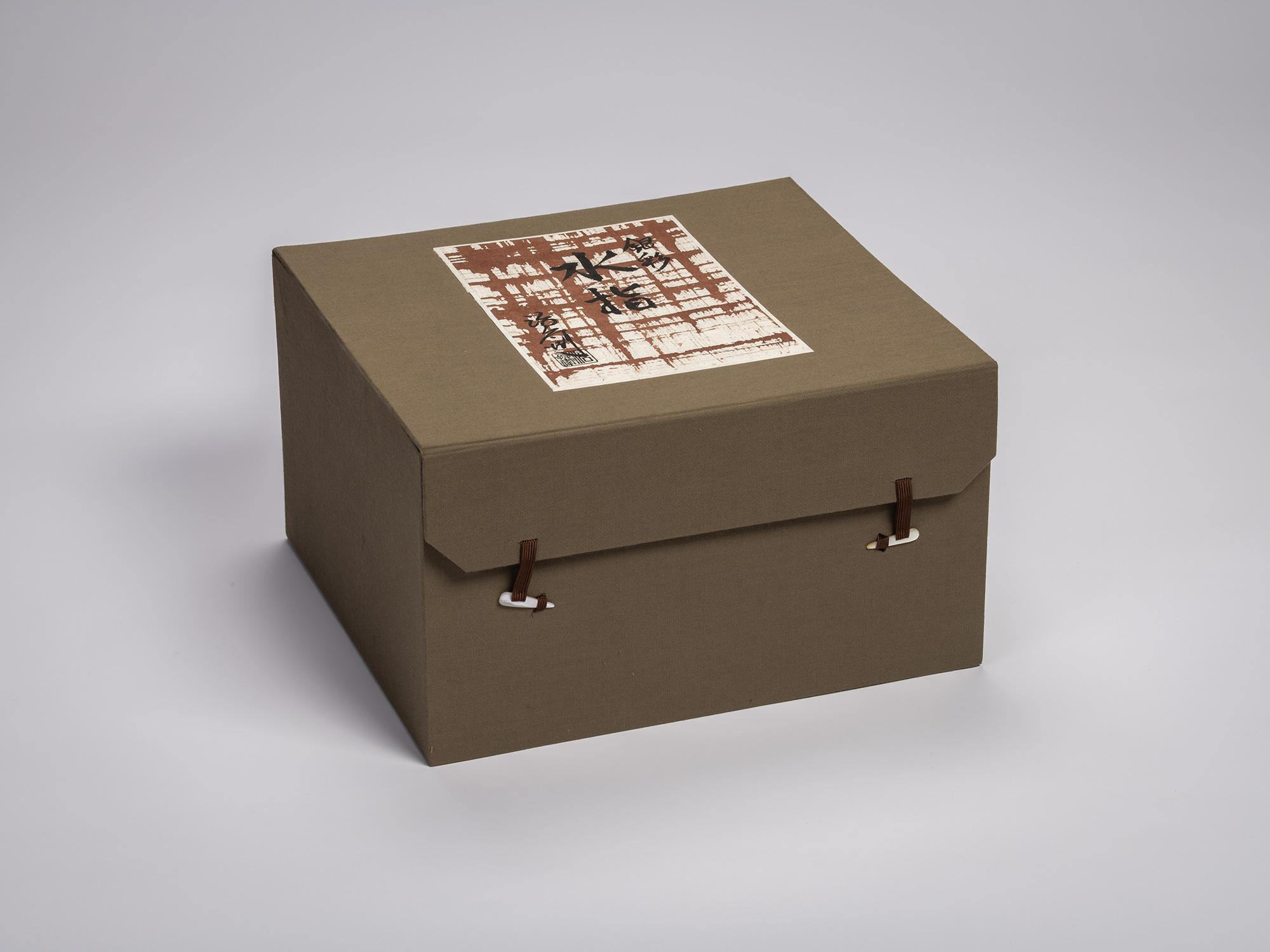 Cloth-covered olive green storage box containing artwork by Jihei Murase, with a paper label on...