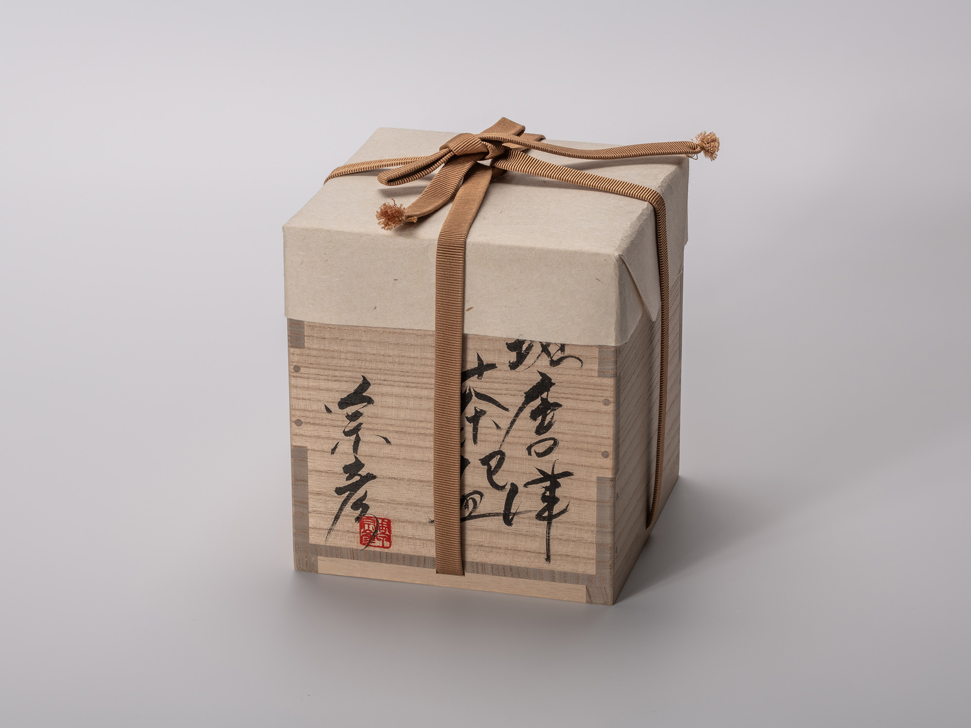 Square wooden tomobako (artist-signed storage box) by ceramic artist, shown with its dark tan fabric...