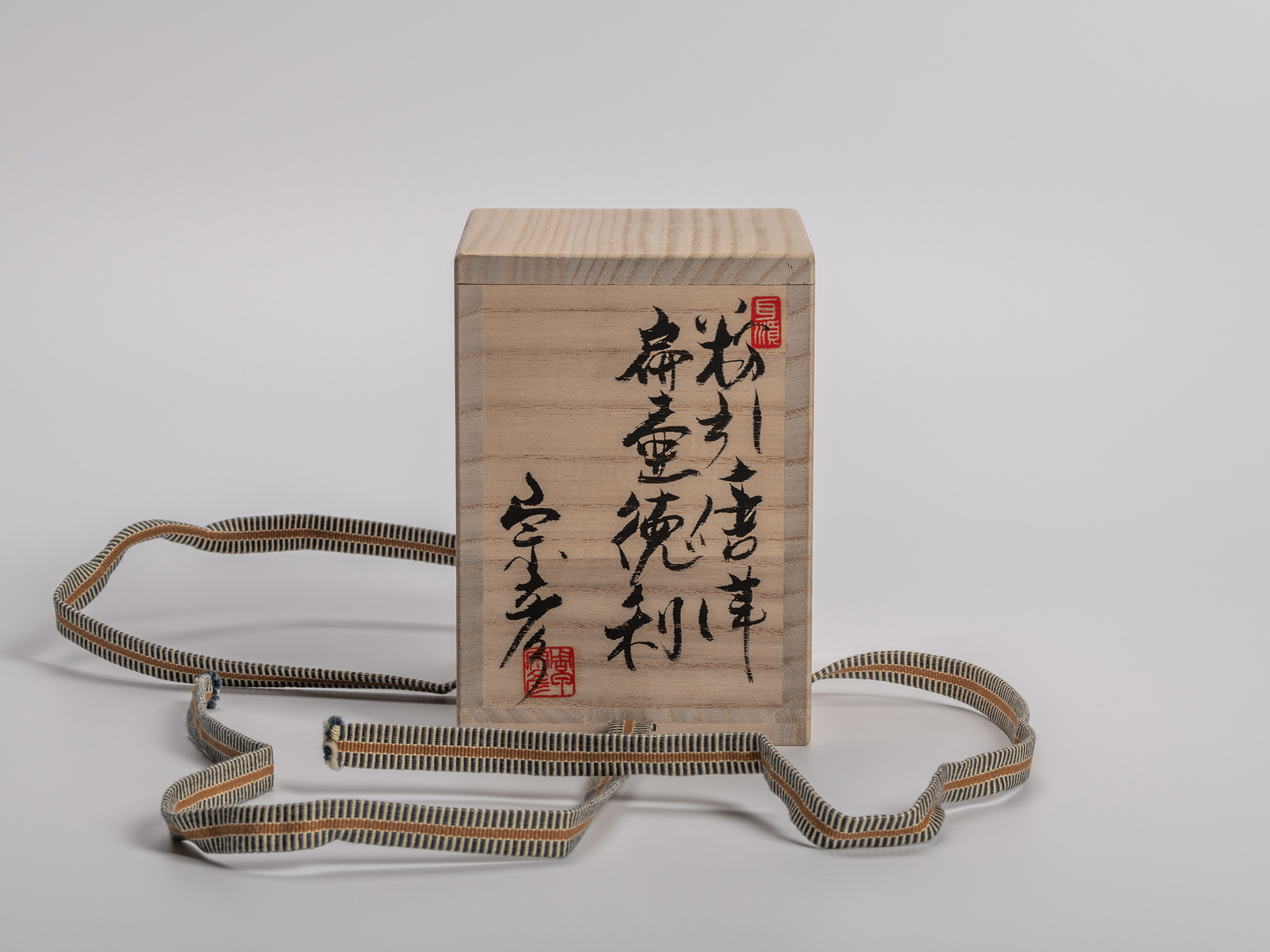 Untied wooden tomobako (signed storage box) shown upright with woven silk cord ties resting in...