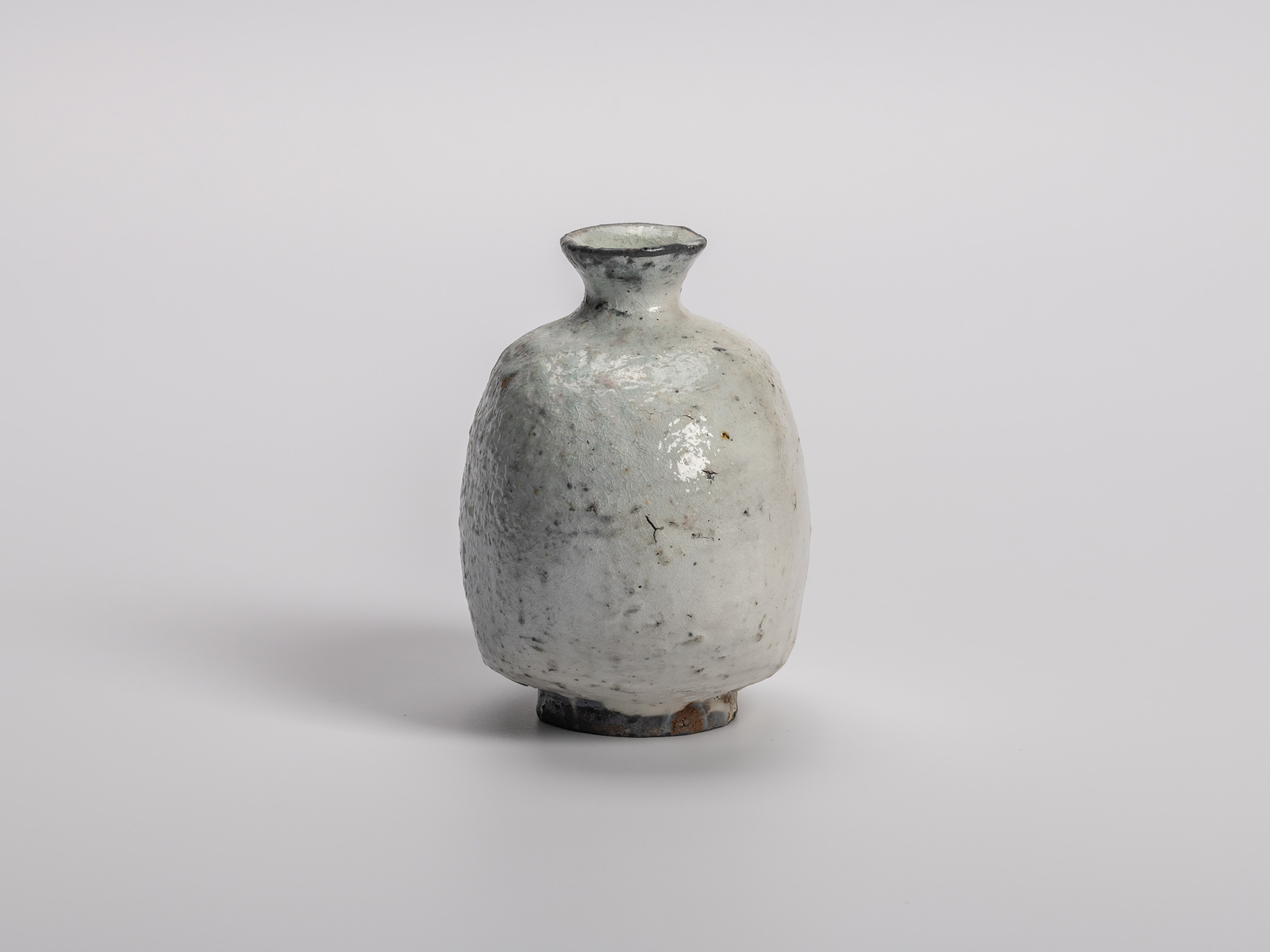 Side profile view of Haikaburi tokkuri (sake bottle) with a rounded, bulbous body that is flattened...