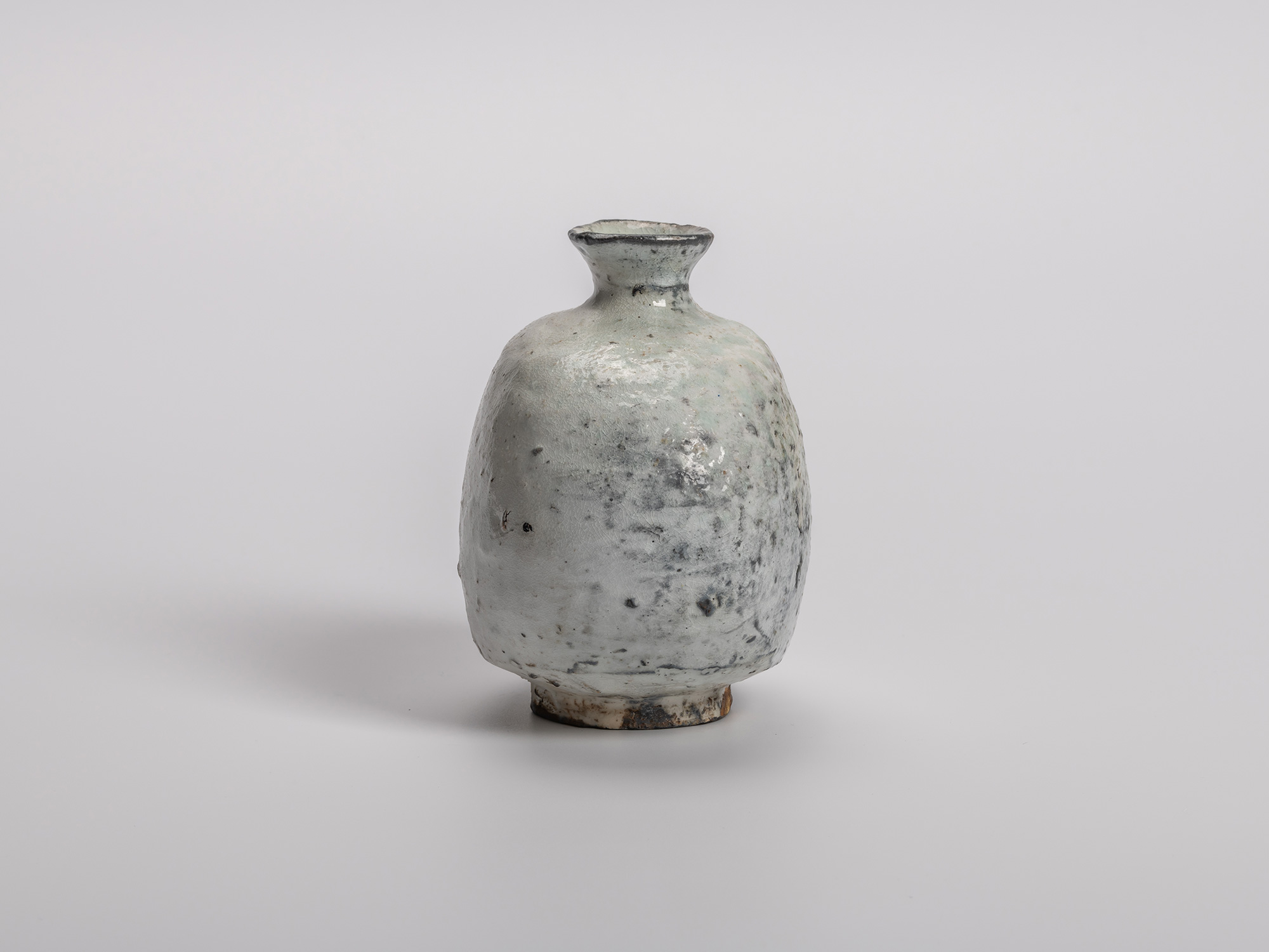 Side profile view of Haikaburi tokkuri (sake bottle) with a rounded, bulbous body that is flattened...