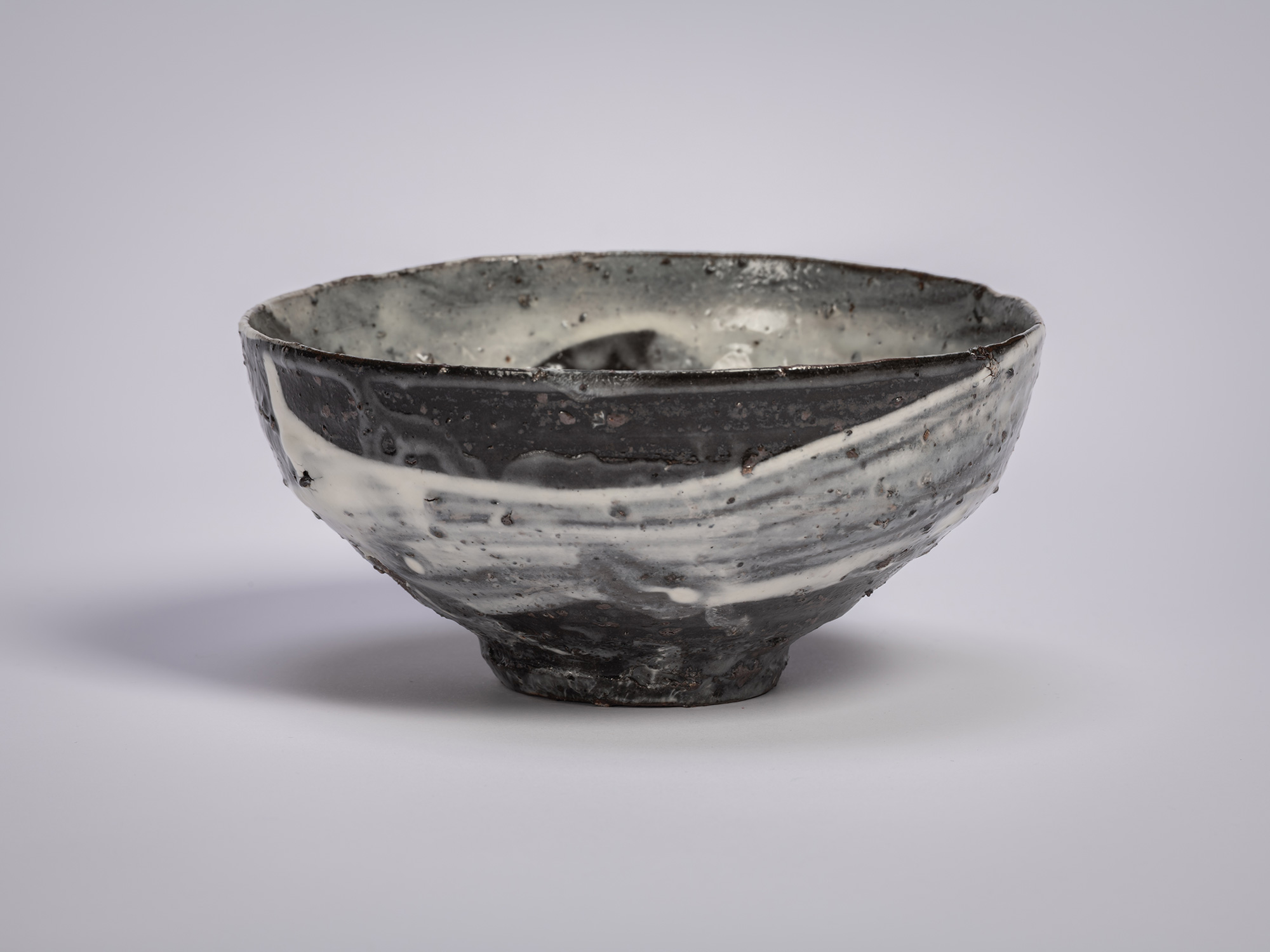 Hakeme tea bowl by Shiro Tsujimura, shown in profile, with a broad, gently flared form and a dark...