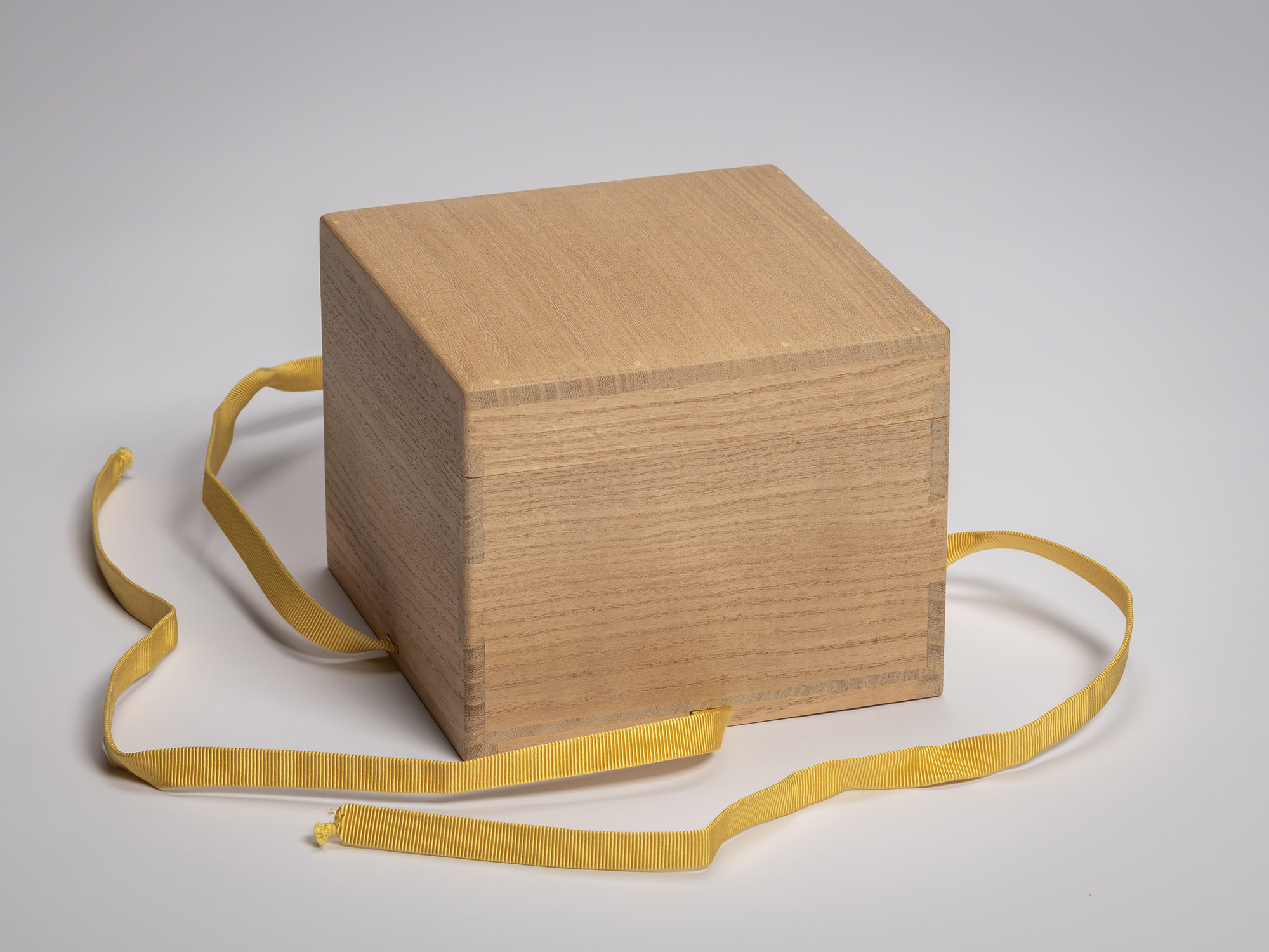 Square wooden tomobako with untied mustard fabric ribbon.