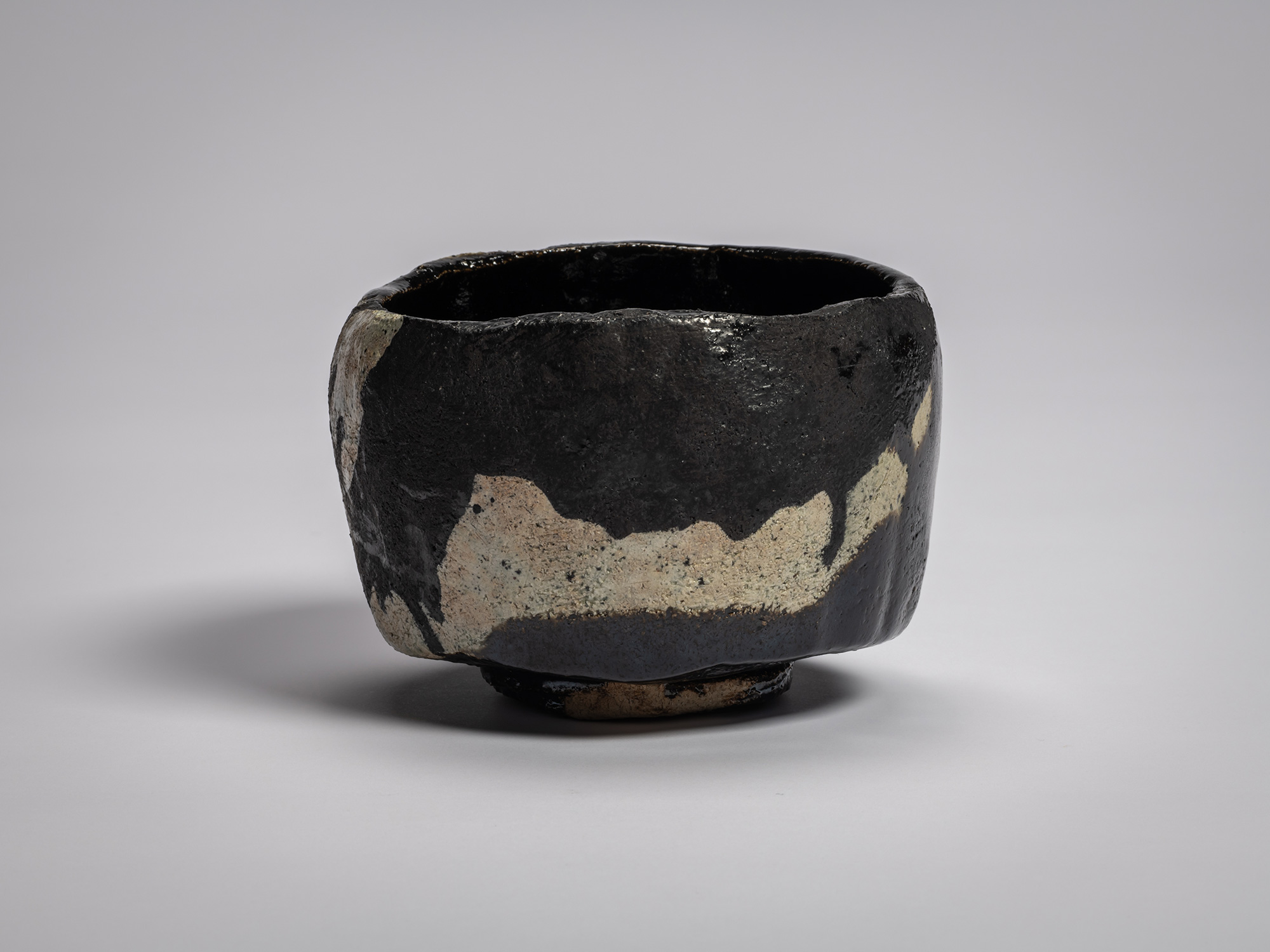 Black Raku tea bowl titled Old Plum Tree, with irregular hand-formed rim, matte black glaze, with...