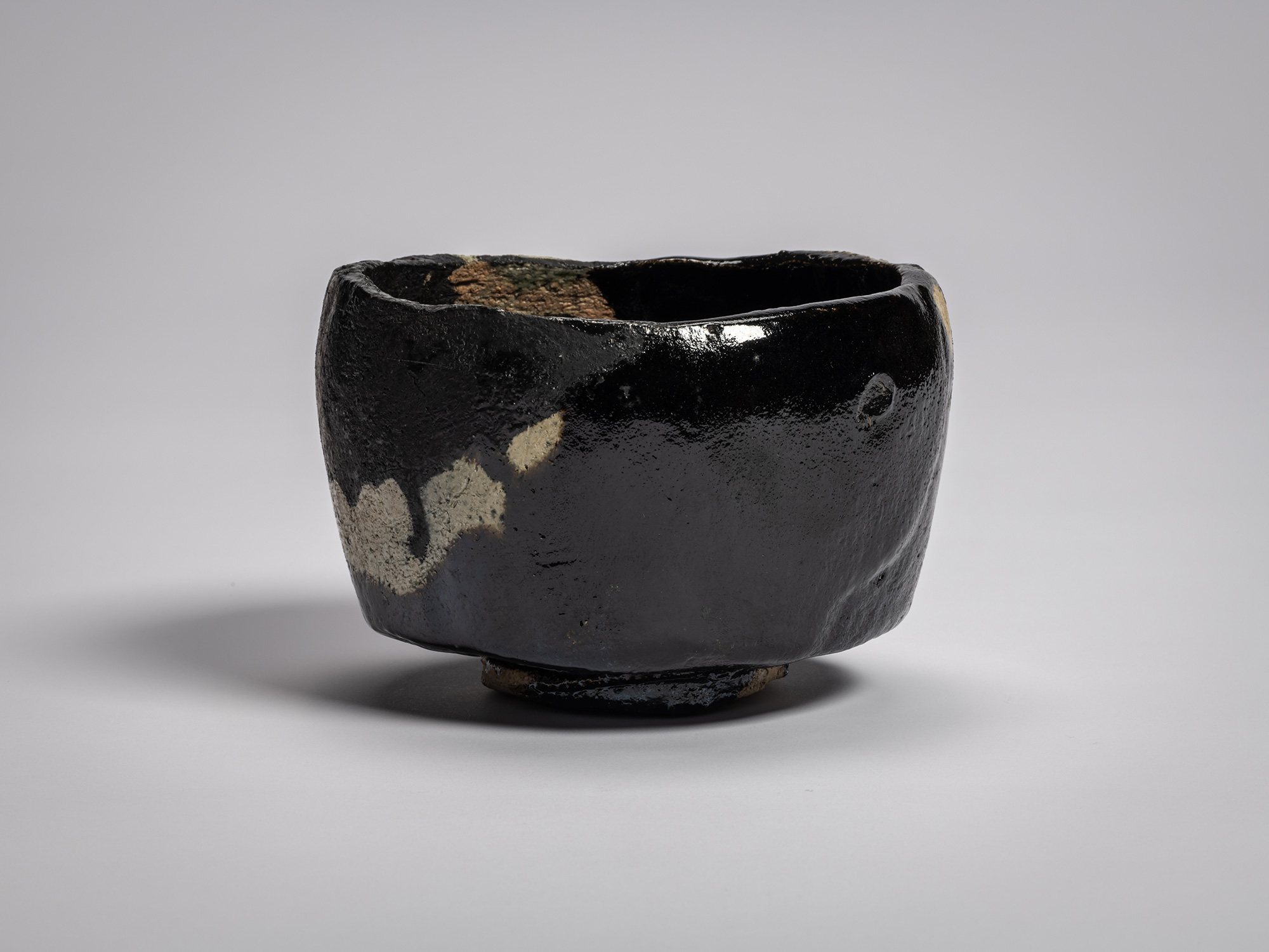 Black Raku tea bowl titled Old Plum Tree, with irregular hand-formed rim, matte black glaze over...