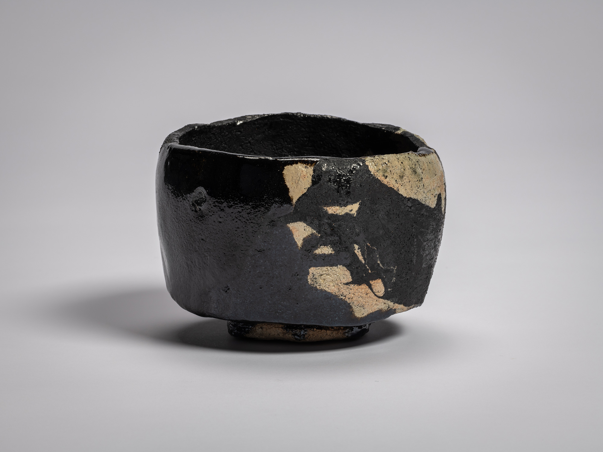 Black Raku tea bowl titled Old Plum Tree, with irregular hand-formed rim, matte black glaze over...