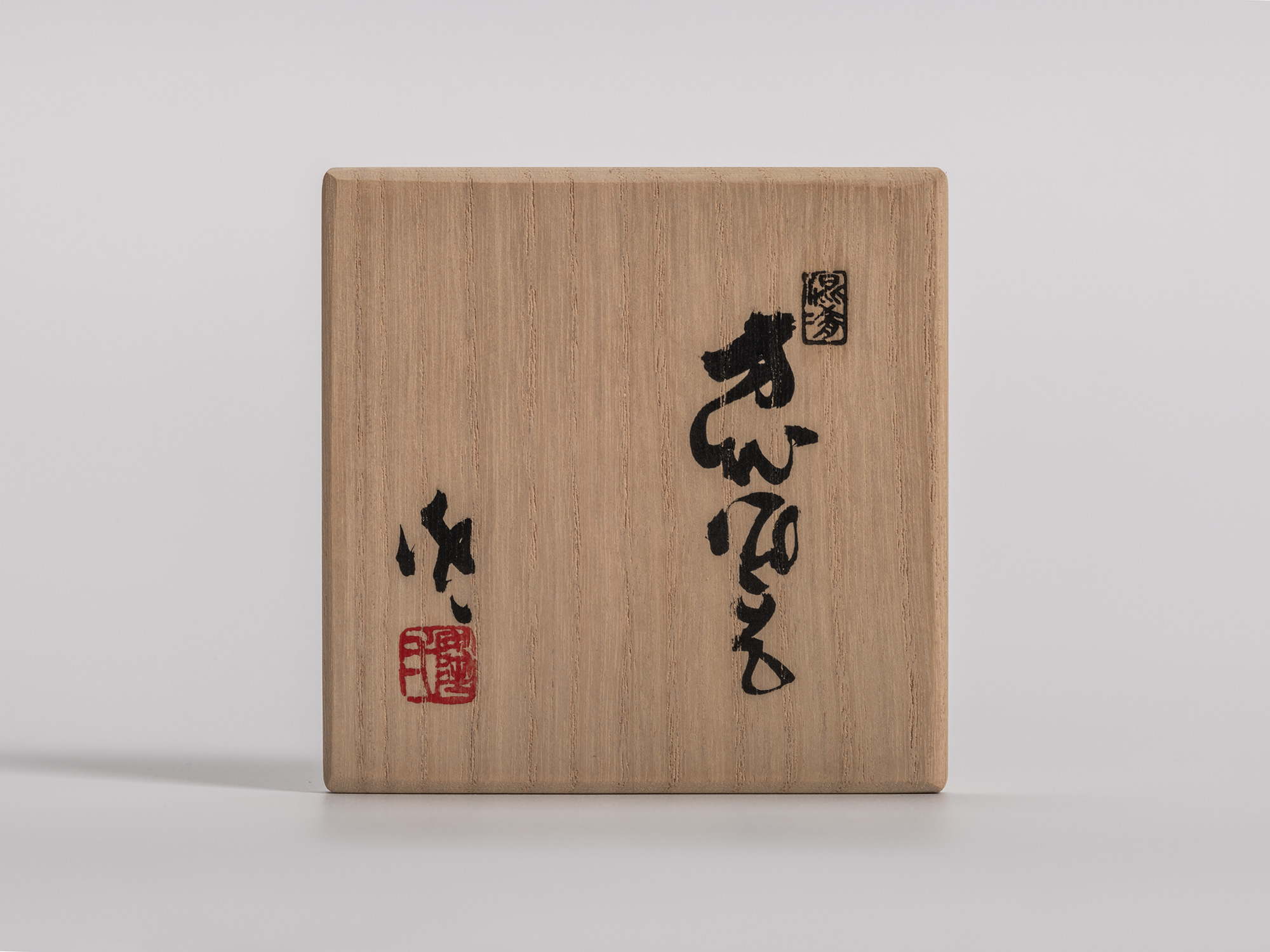 Wooden tomobako box lid for a guinomi sake cup by Kakurezaki Ryūichi, featuring bold black calligraphy...