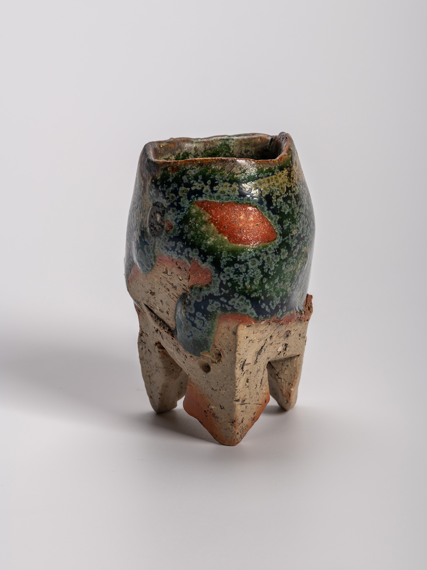 Iron Oribe sake cup with irregular faceted form, copper-green glaze, and iron-rich clay body, showing...
