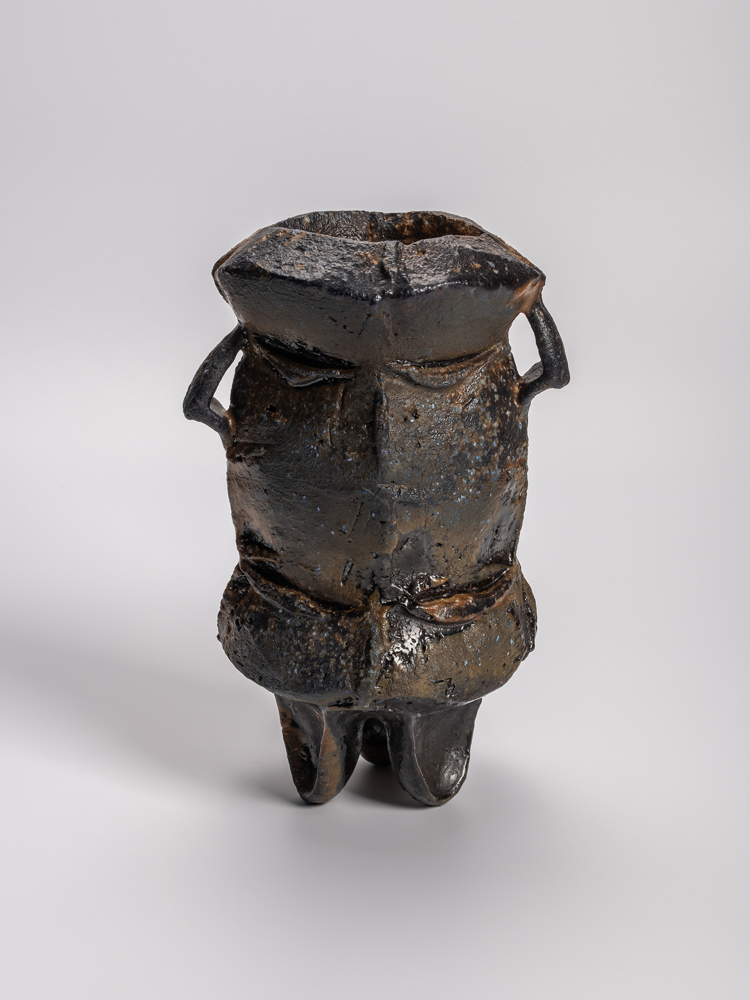 Black three-legged ceramic vase title by Kakurezaki Ryūichi, featuring a rugged, sculptural form...