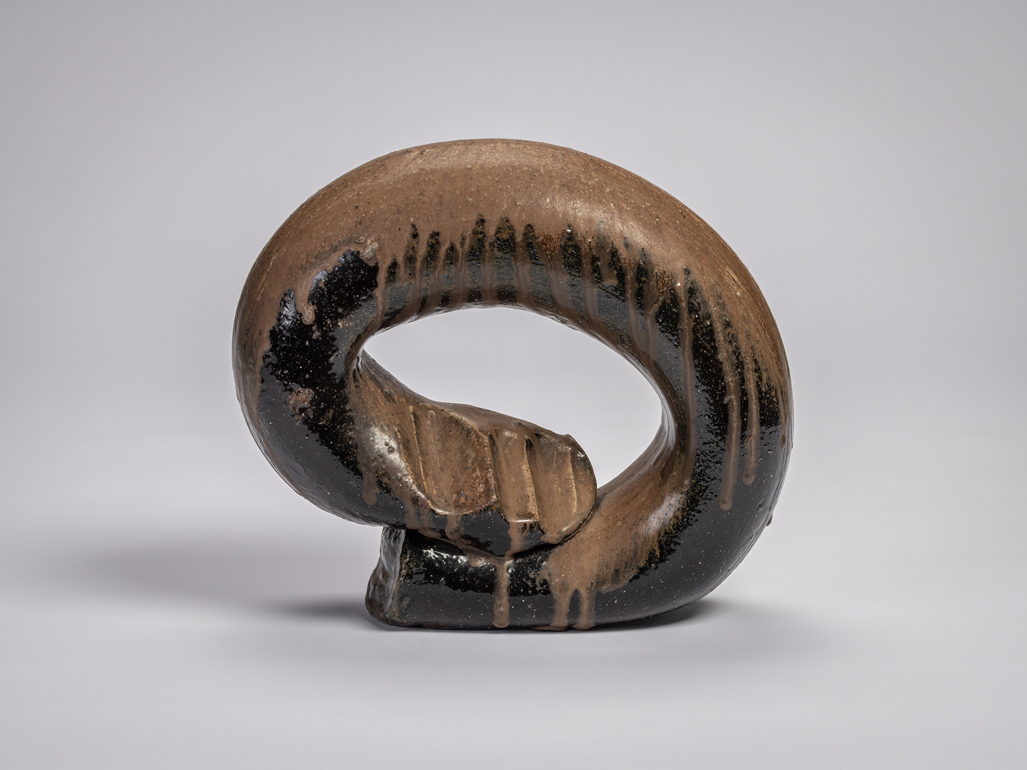 Front view of the ceramic sculpture Ring by Jun Isezaki, featuring a dark thick circular form with...