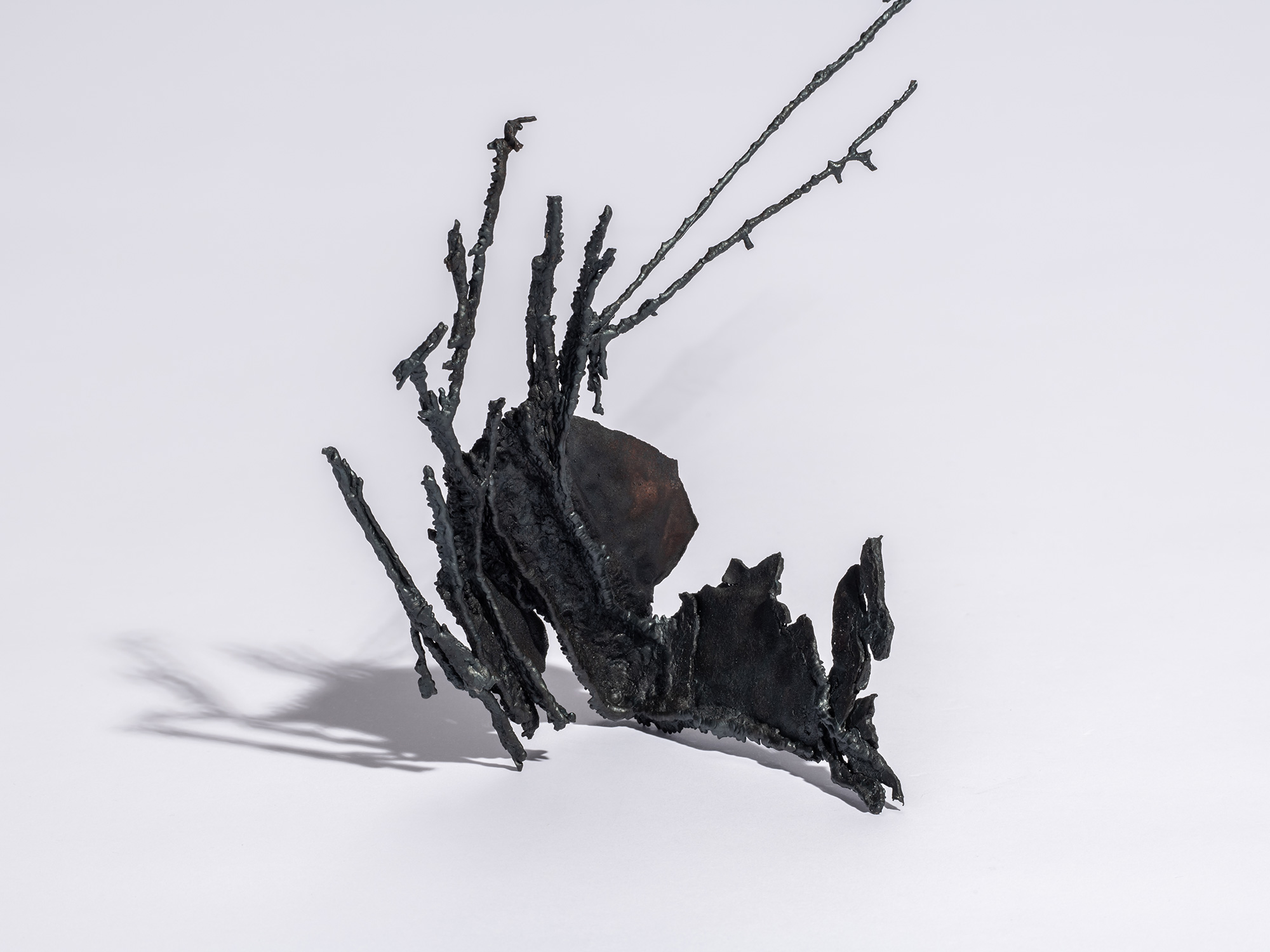 Detail of iron sculpture Sai by Aki Rusu, featuring a clustered, organic base of dark oxidized...