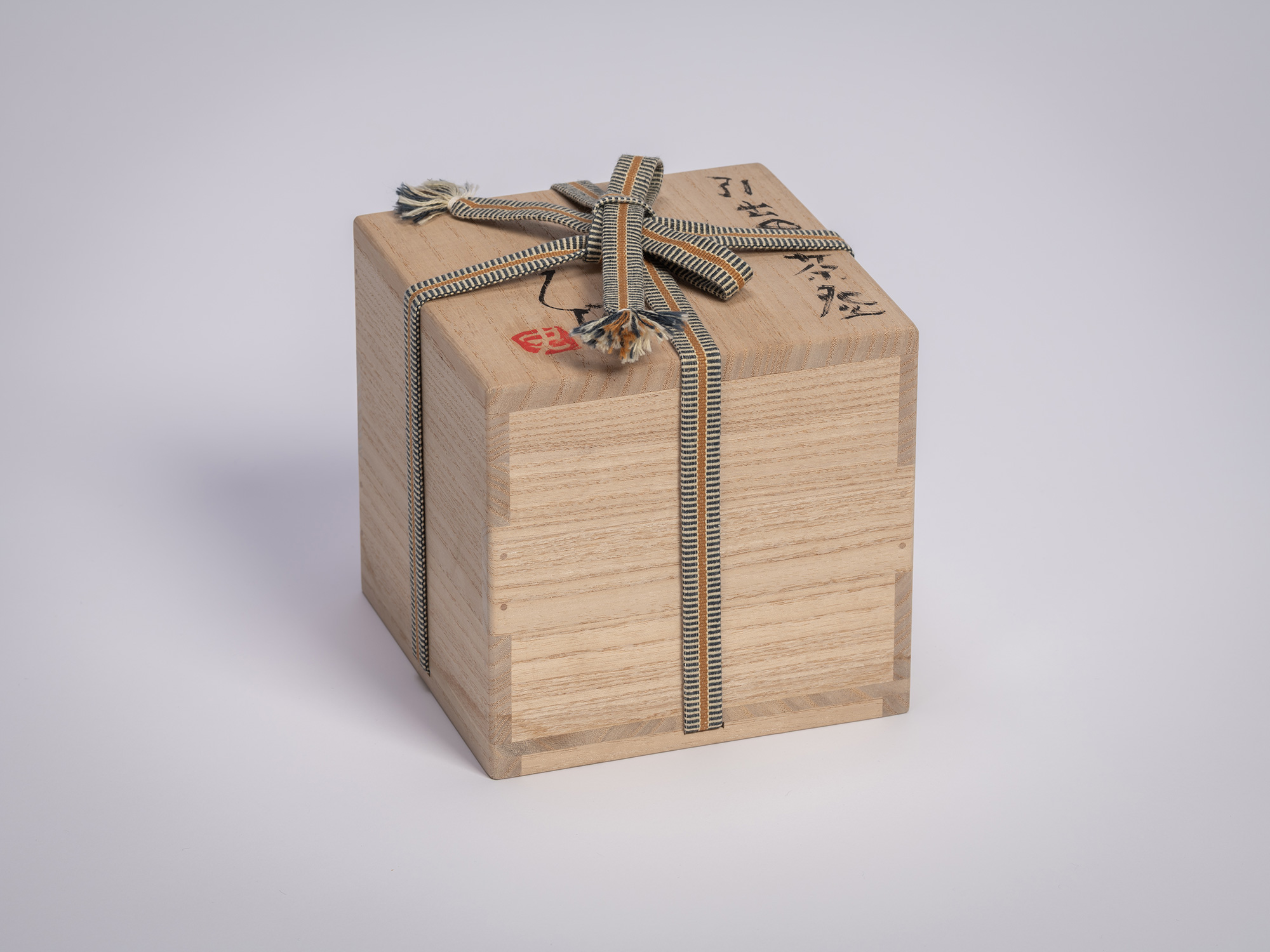 Wrapped wooden tomobako box containing a tea bowl by Shiro Tsujimura, secured with a woven cord...