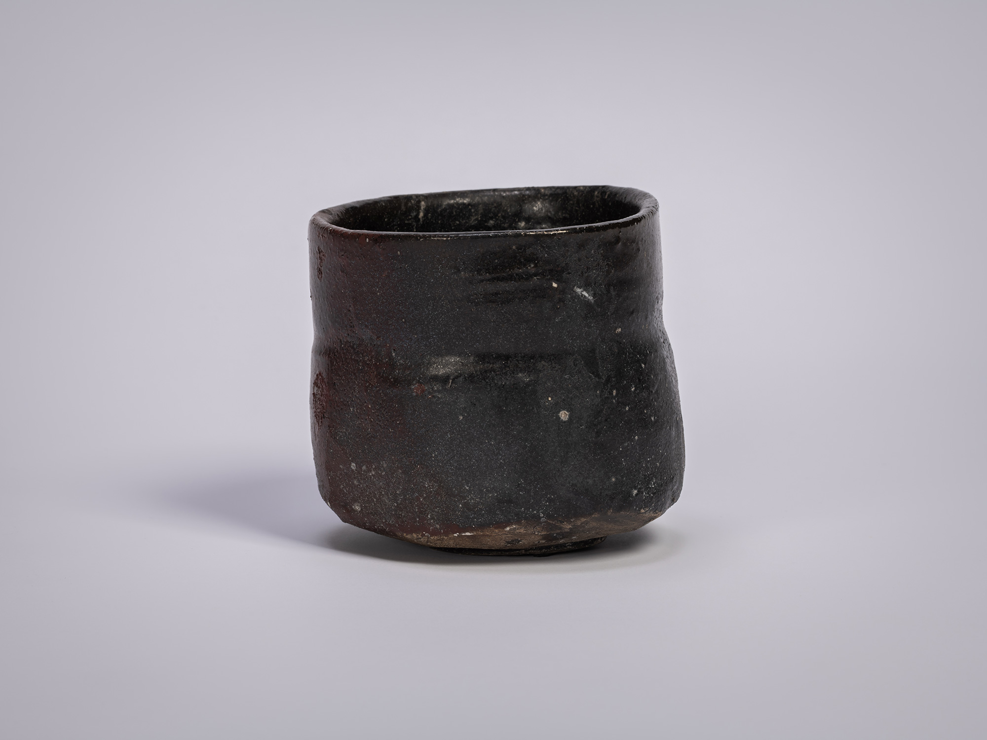 Stoneware tea bowl by Shiro Tsujimura, featuring a cylindrical form with dark, fire-marked surface,...