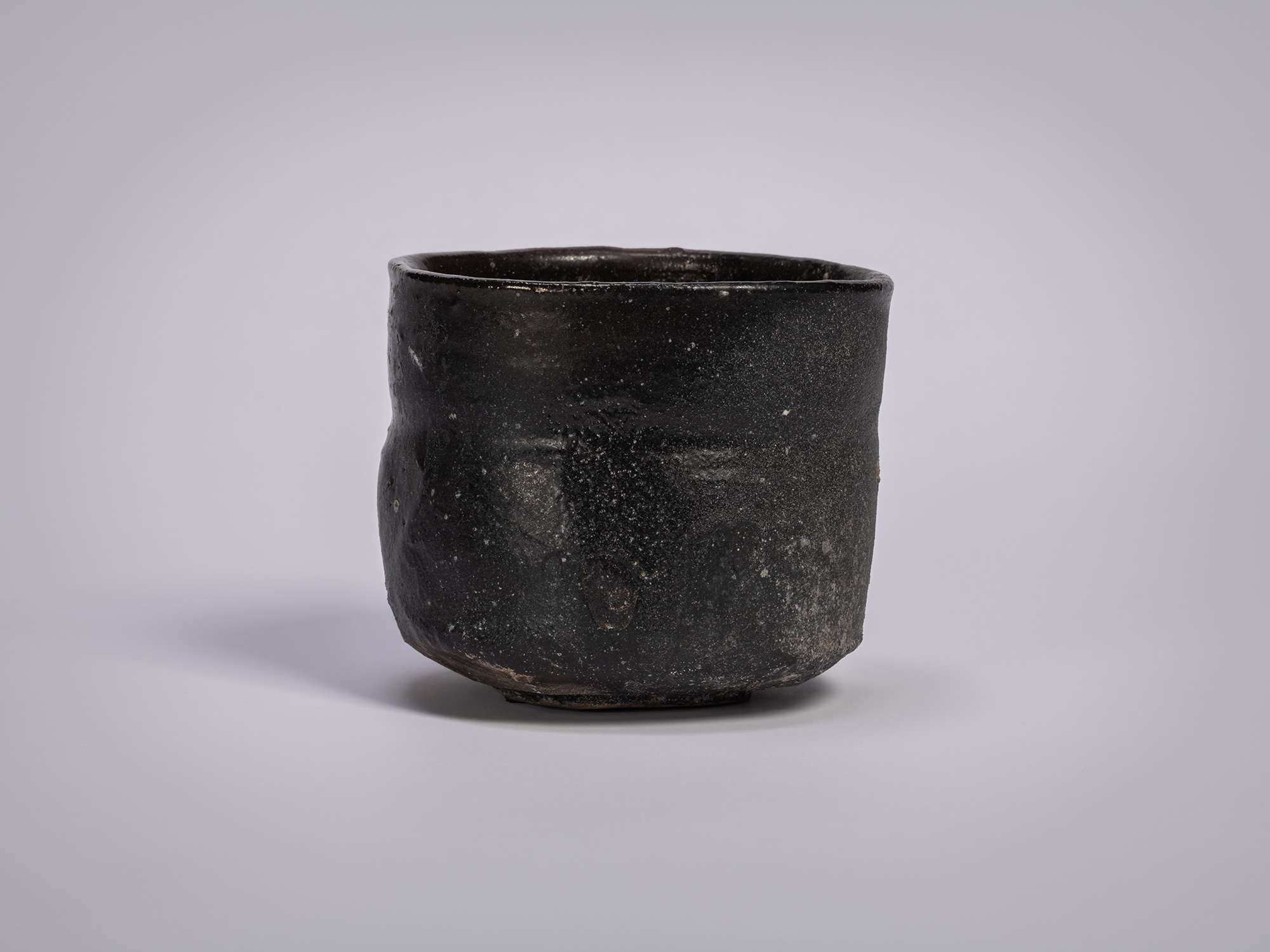 Stoneware tea bowl by Shiro Tsujimura, featuring a cylindrical form with dark, fire-marked surface,...