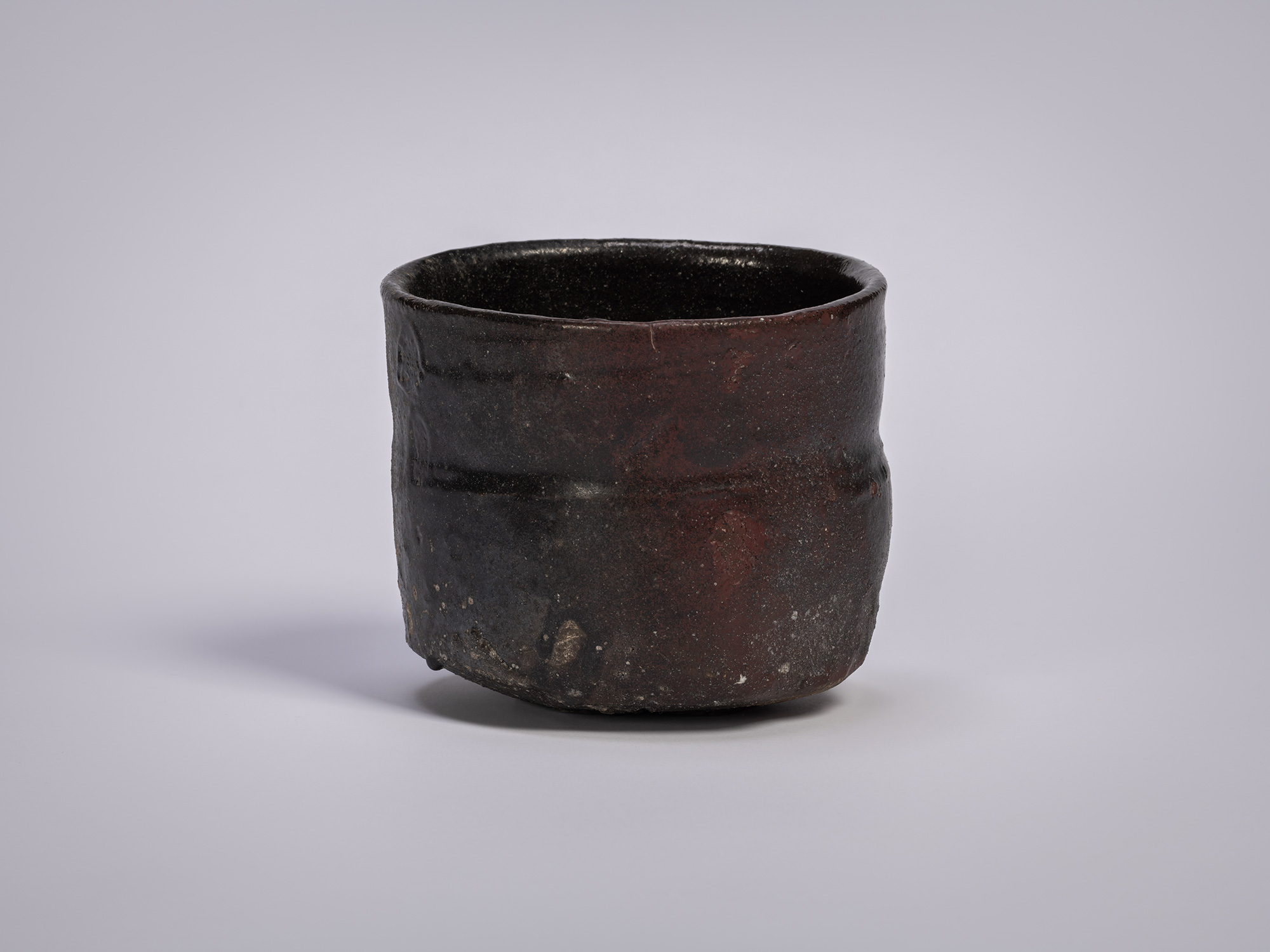 Stoneware tea bowl by Shiro Tsujimura, featuring a cylindrical form with dark, fire-marked surface,...