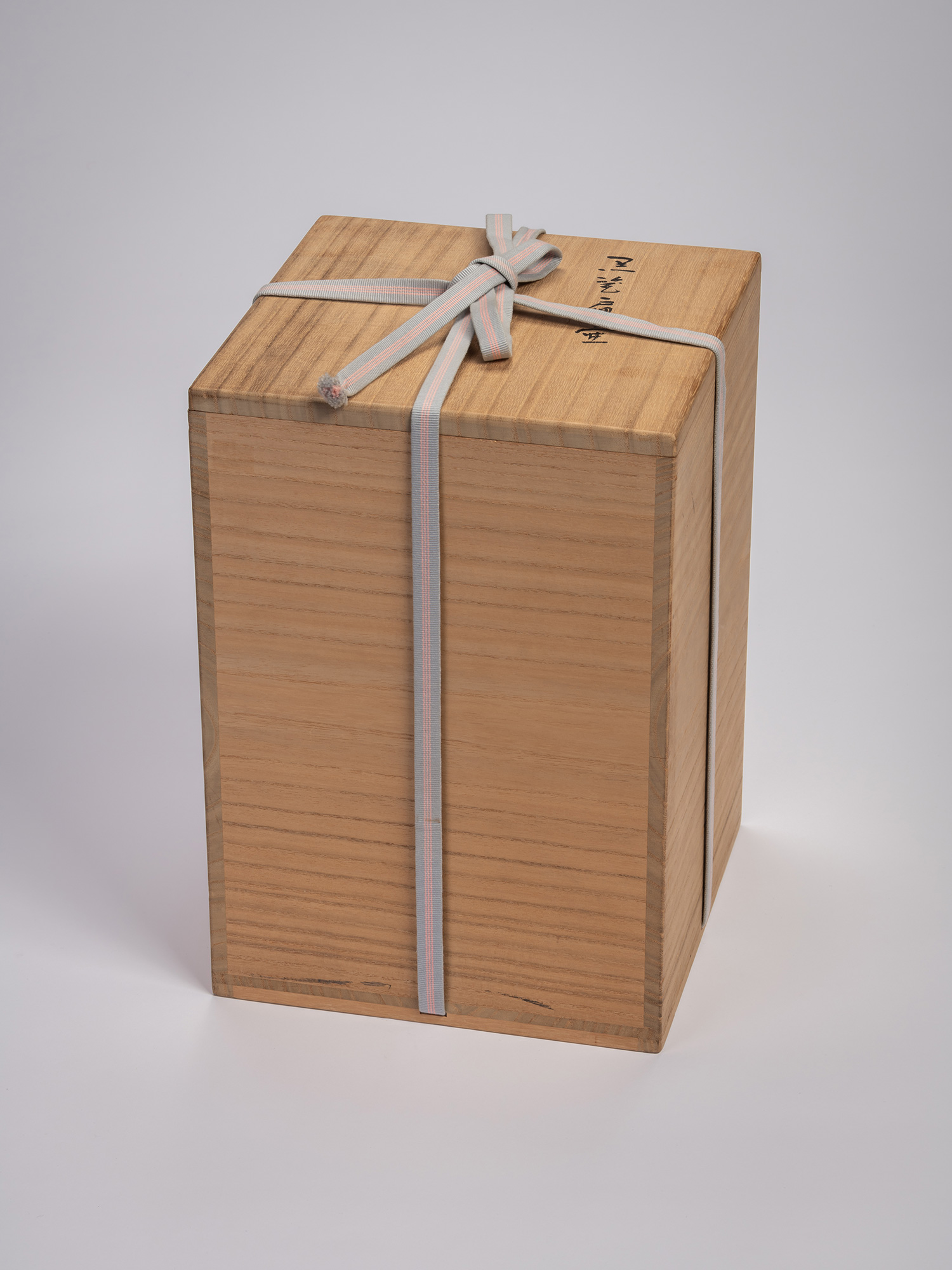Closed wooden tomobako storage box tied with a gray-and-pink cord, housing a black stoneware triangular...