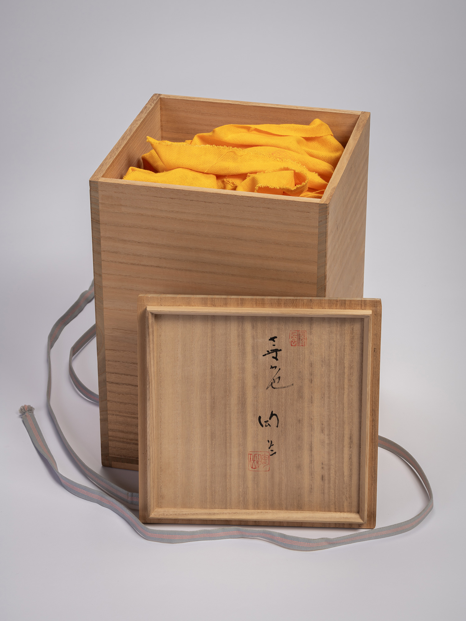 Wooden tomobako (storage box) with lid removed, containing yellow cloth wrapping a black stoneware...