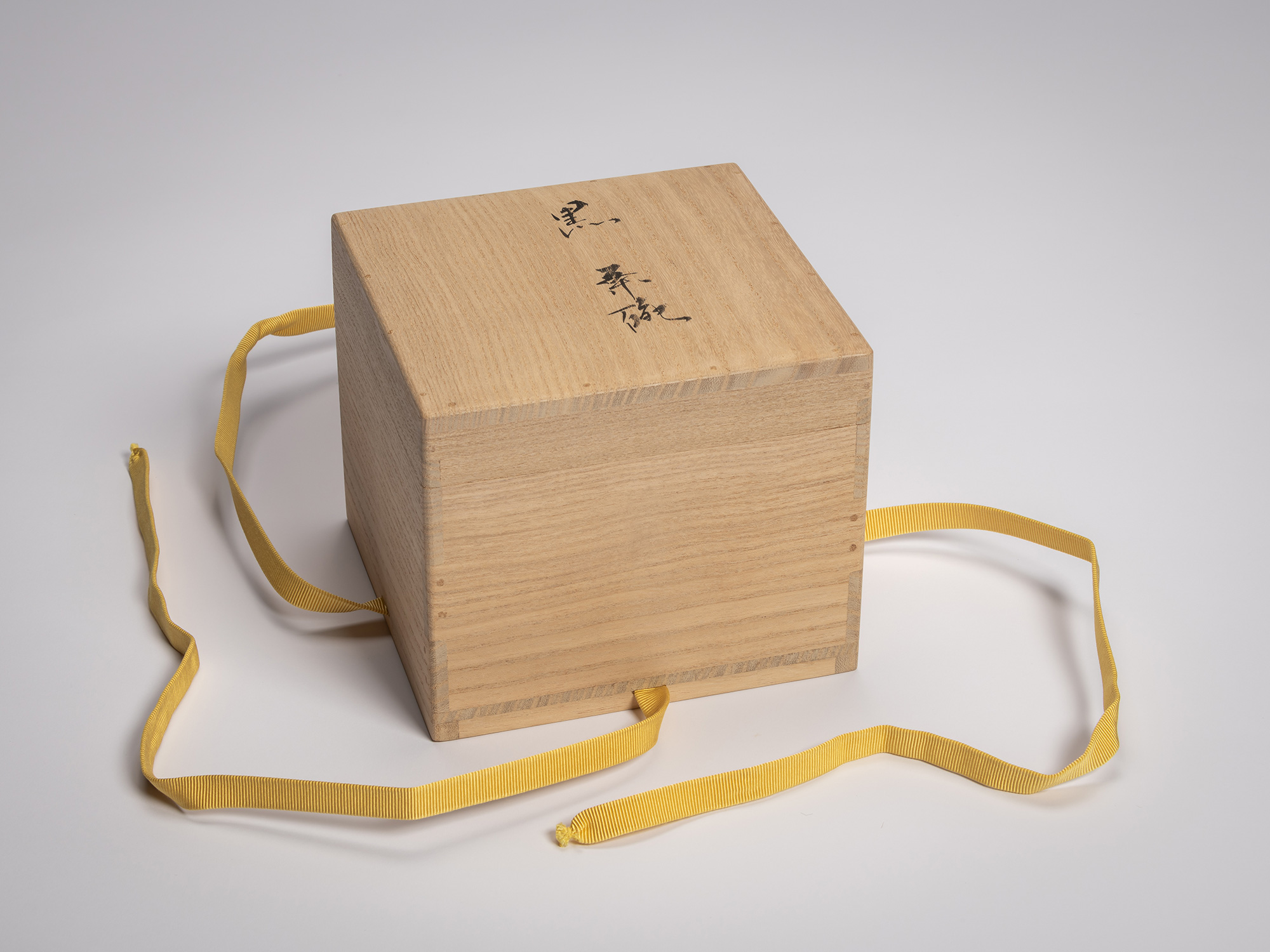 Exterior lid of a wooden tomobako for a Black Raku tea bowl, tied with a yellow cord, inscribed...