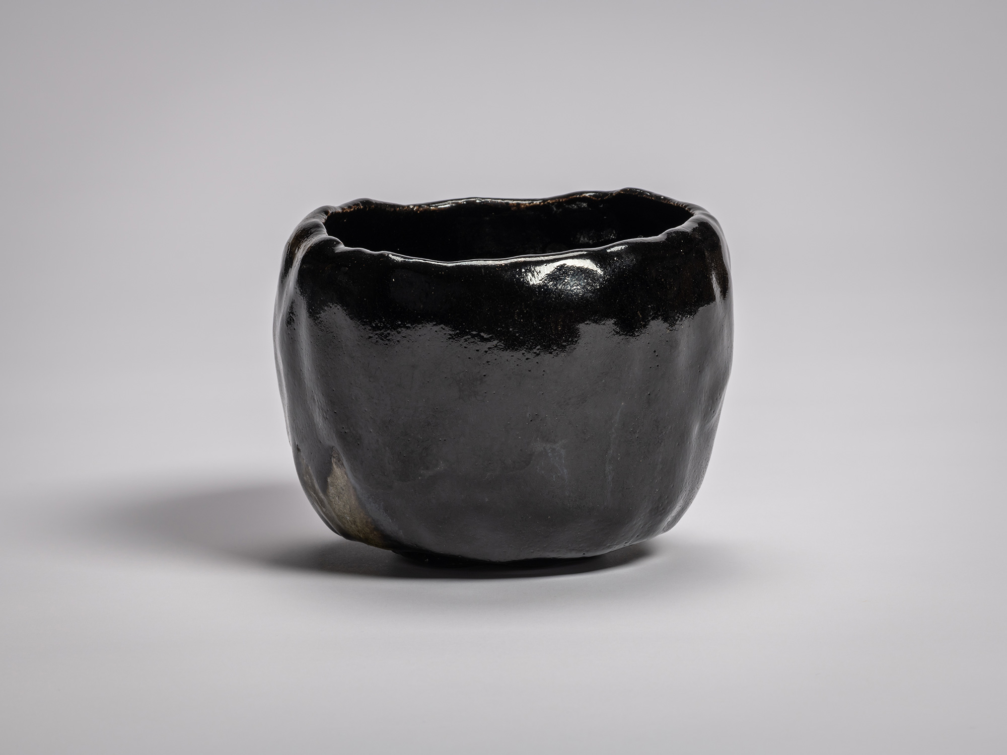 Black Raku tea bowl by Raku XV with a softly undulating rim, deep glossy black glaze, and subtle...