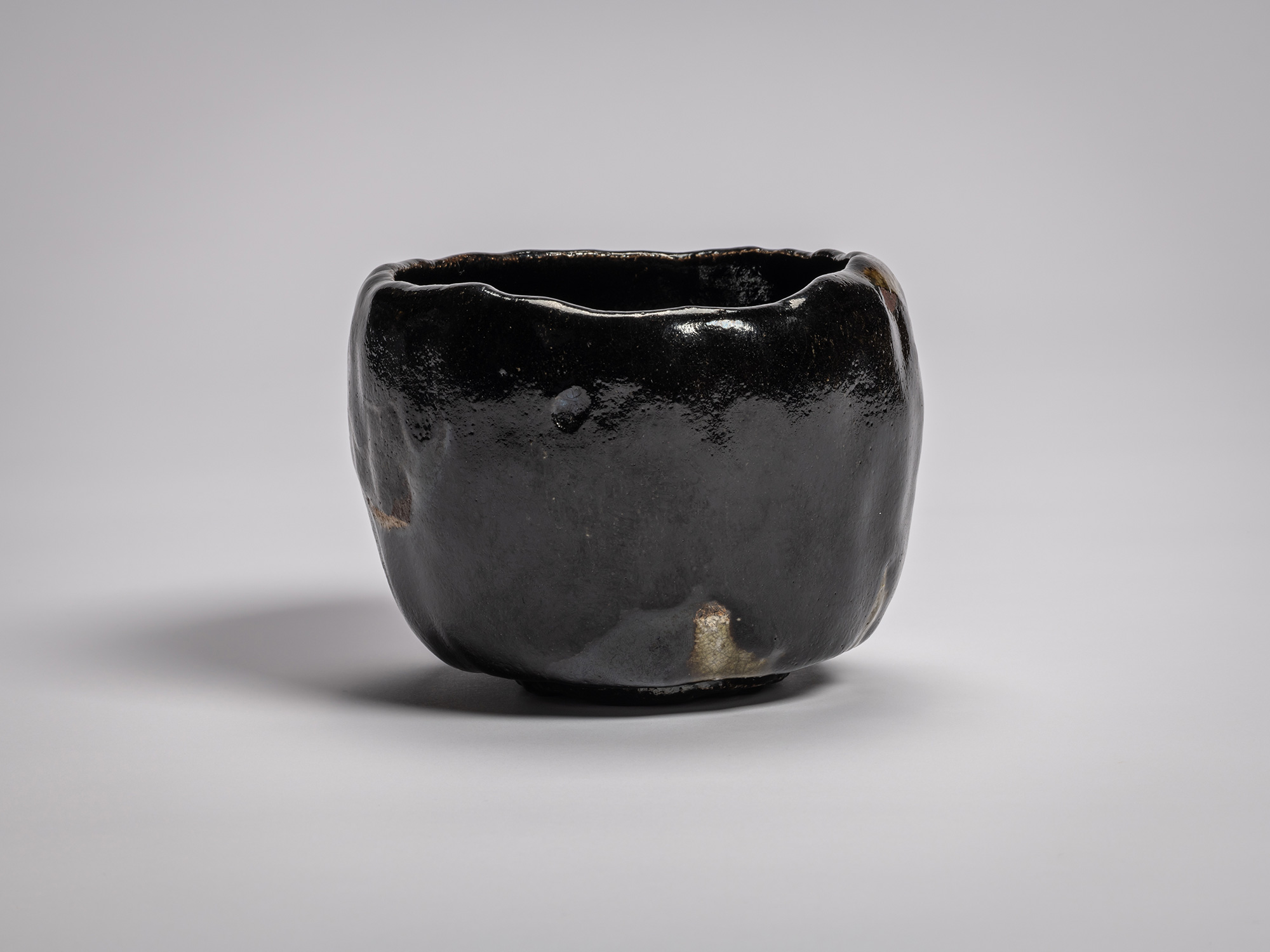 Black Raku tea bowl by Raku XV with a softly undulating rim, deep glossy black glaze, and subtle...