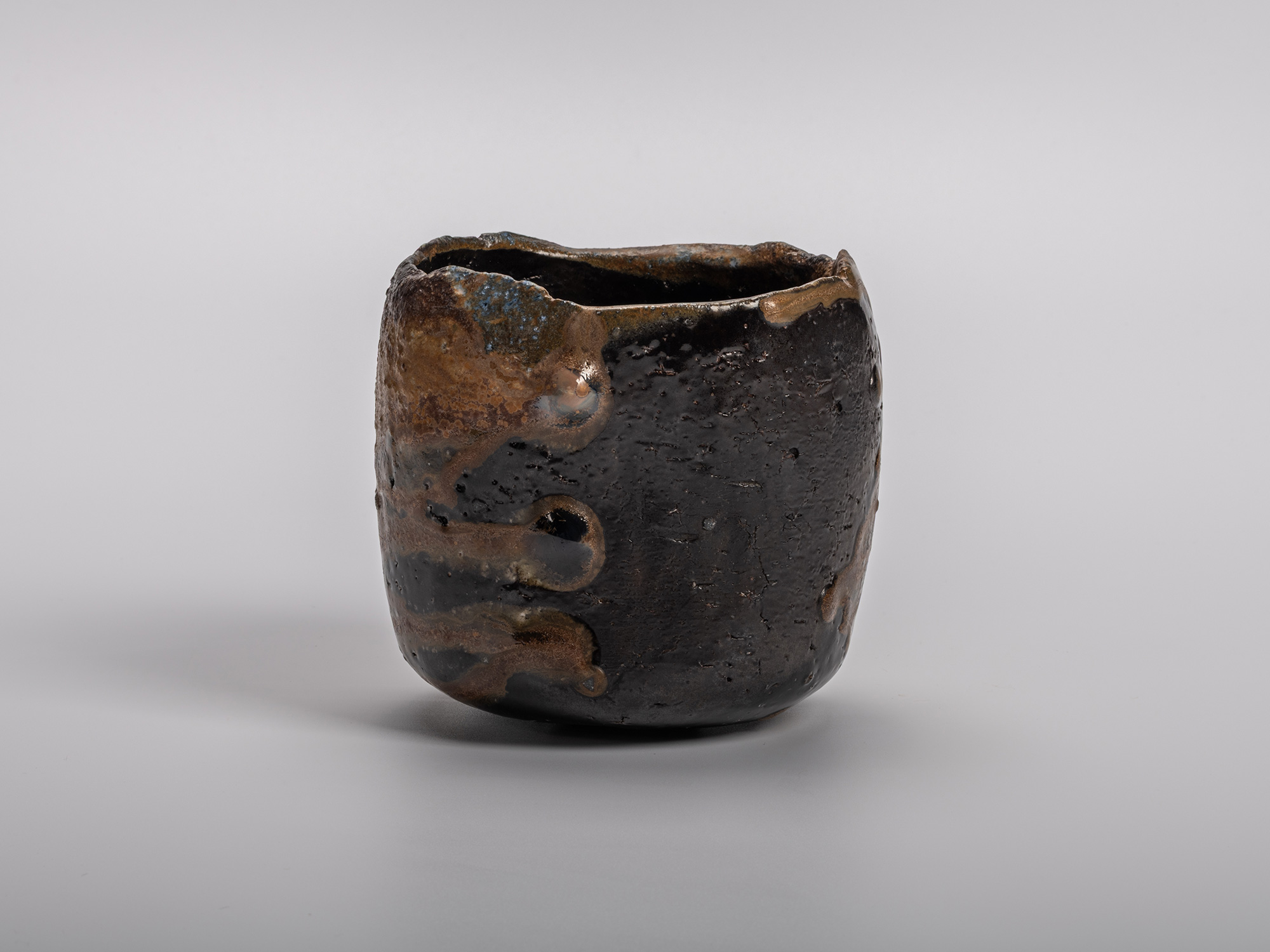 Black tea bowl by Kakurezaki Ryūichi with a sculptural cylindrical form, irregular rim, and richly...