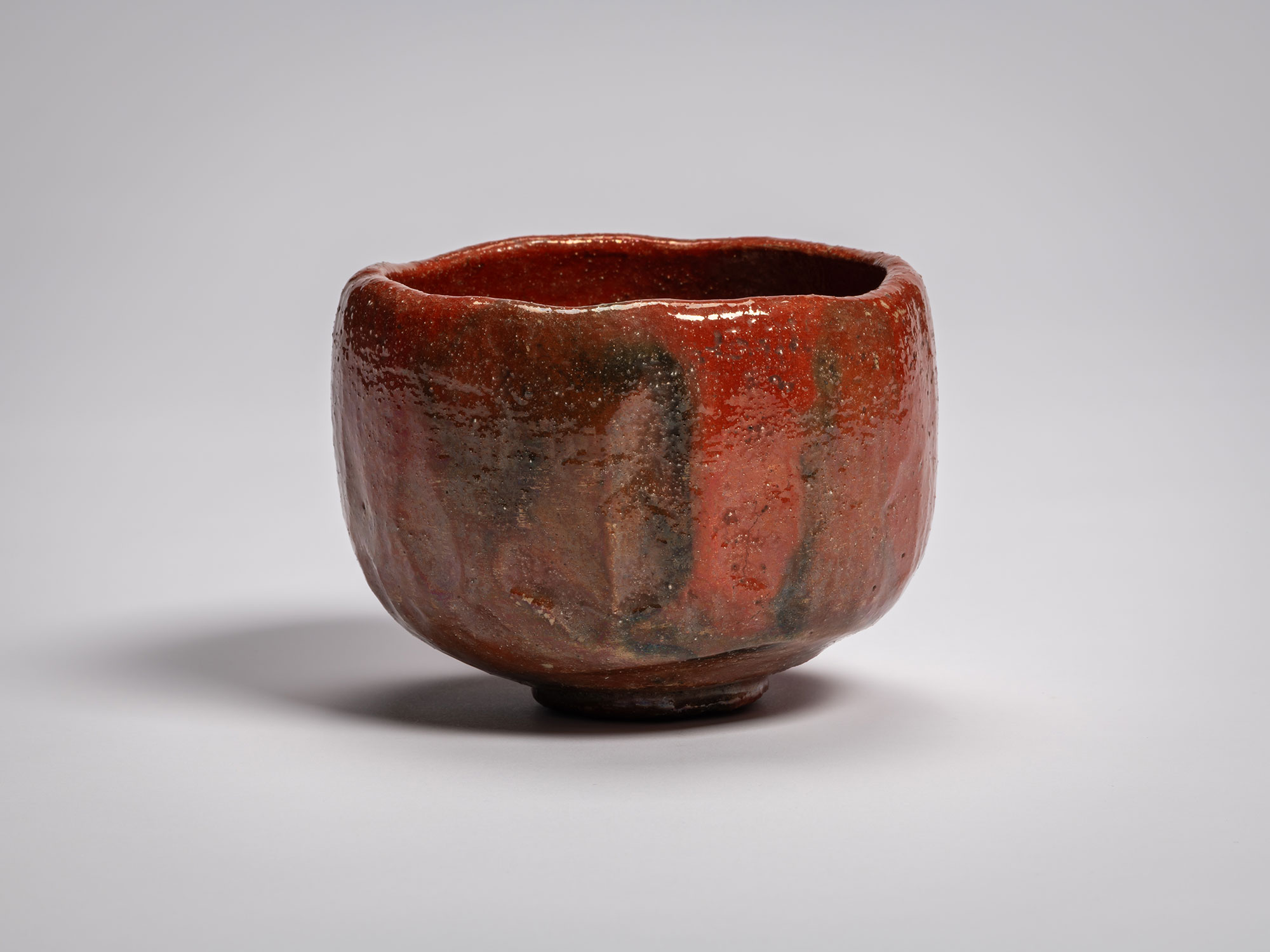 Profile view of the Daiyūhō (Great Peak) red Raku tea bowl, featuring a hand-sculpted, cylindrical...