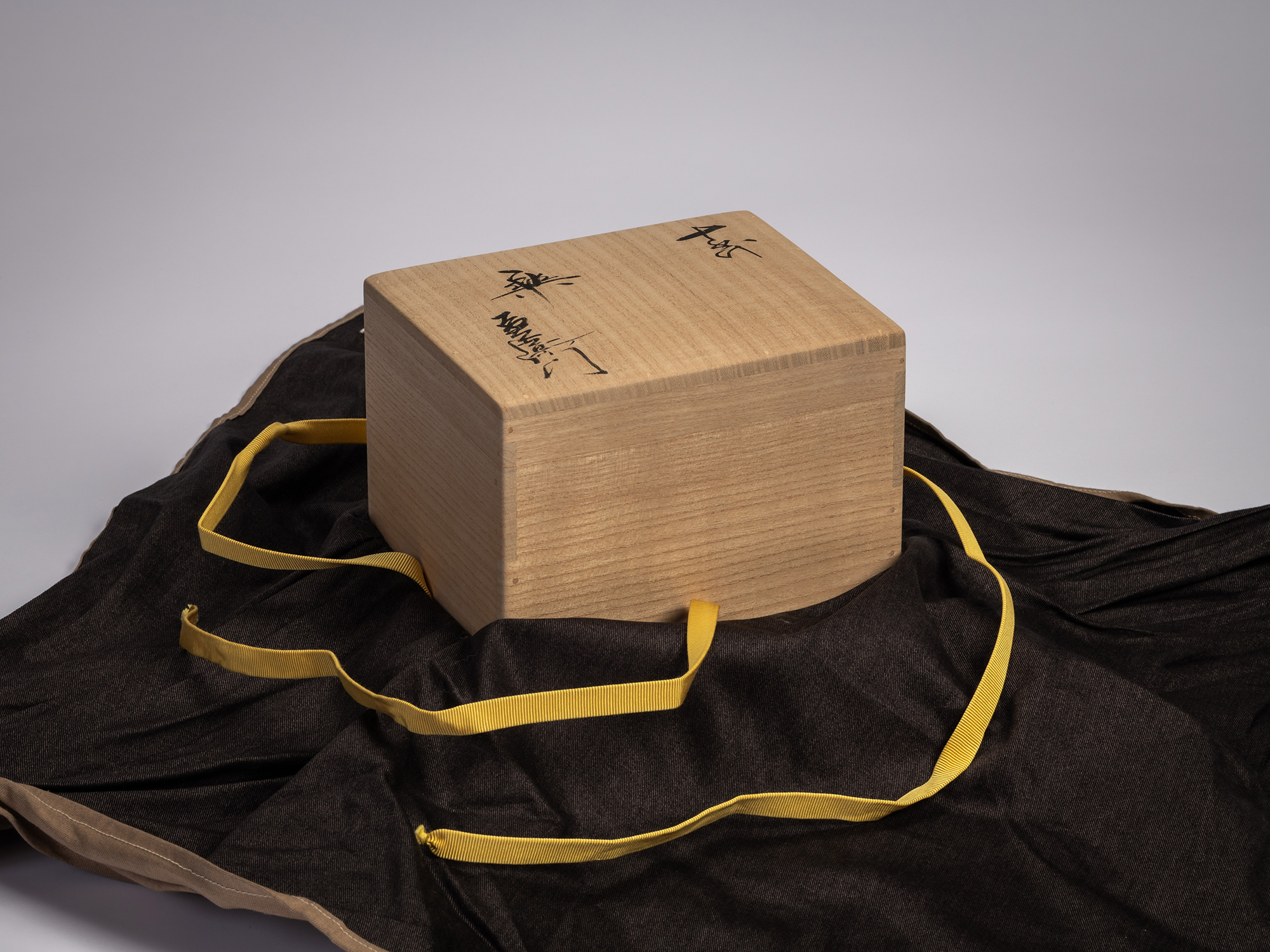 Wooden artist box containing the tea bowl Gyō by Raku XV (Jikinyū), resting on a dark cloth with...