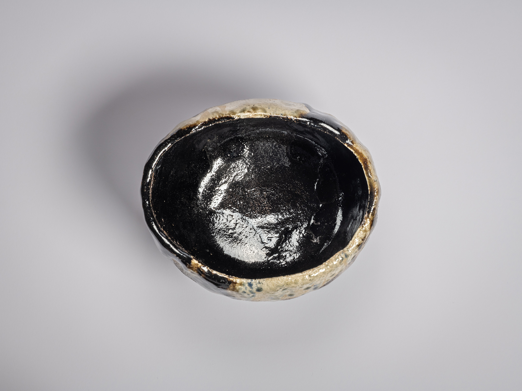 Interior view of a Raku tea bowl with a lustrous black glazed mikomi forming a reflective, pooled...